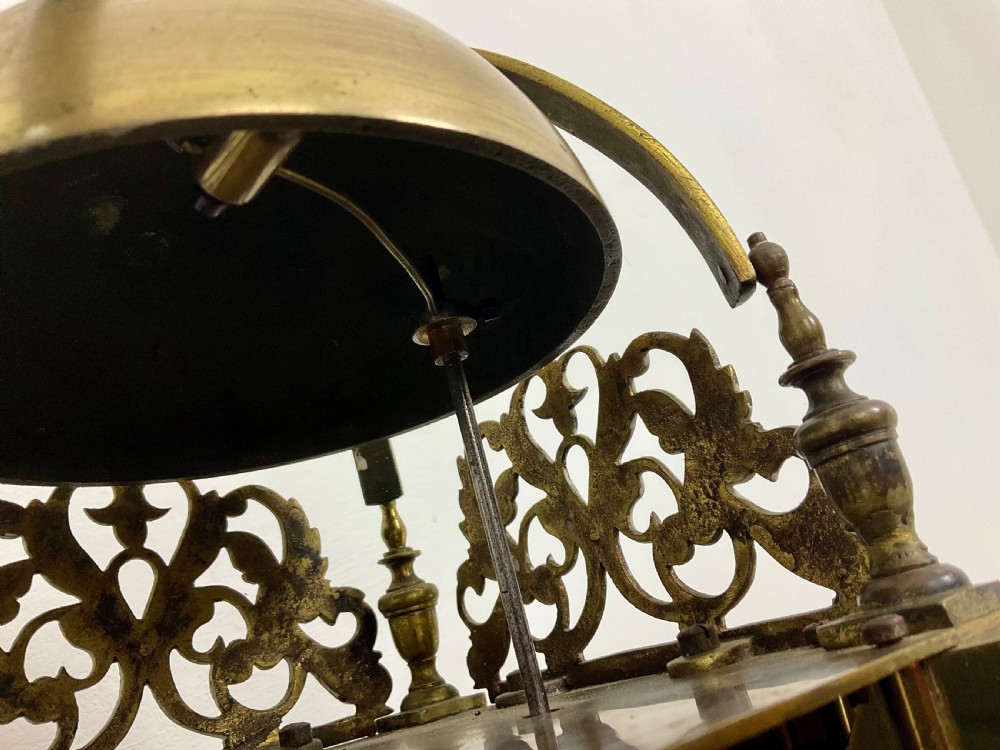 An antique brass lantern clock featuring a top-mounted bell dome, engraved foliate dial with Roman numerals, and ornate pierced frets. View VIII