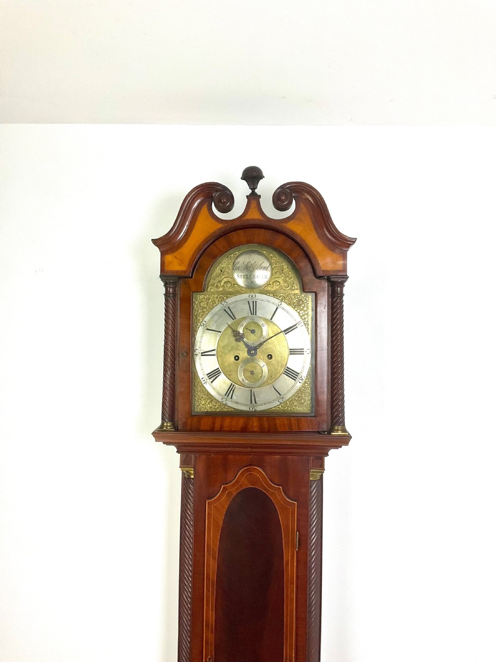 A late Georgian mahogany longcase clock featuring a swan-neck pediment, twisted columns, and an arched dial with silvered chapter ring.