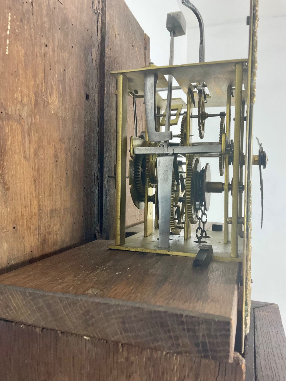 An antique Georgian oak longcase clock hood with a square brass dial, engraved numerals, corner spandrels, and turned side columns. View VI