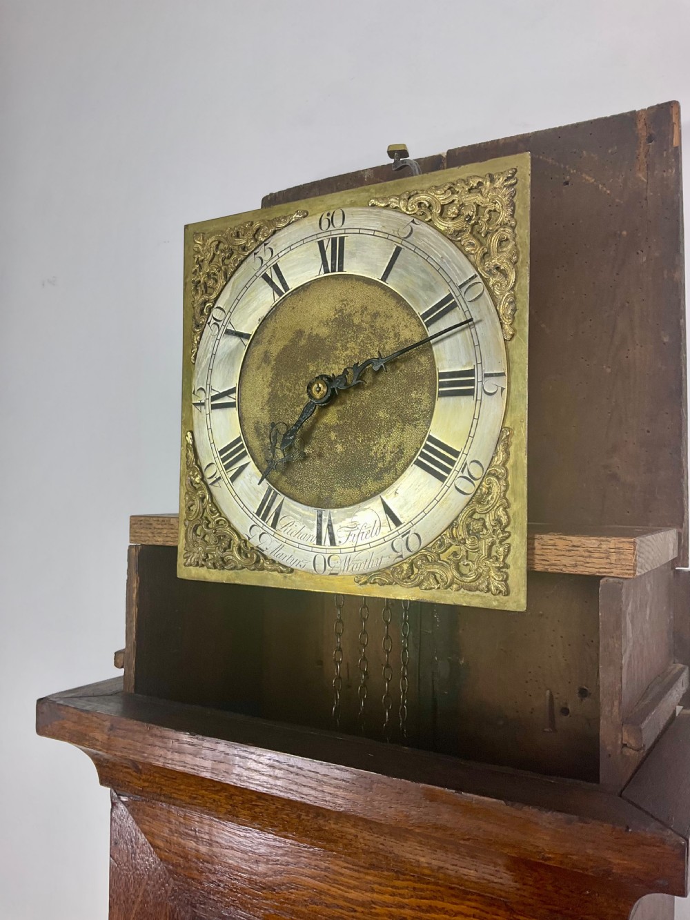 An antique Georgian oak longcase clock hood with a square brass dial, engraved numerals, corner spandrels, and turned side columns. View VII
