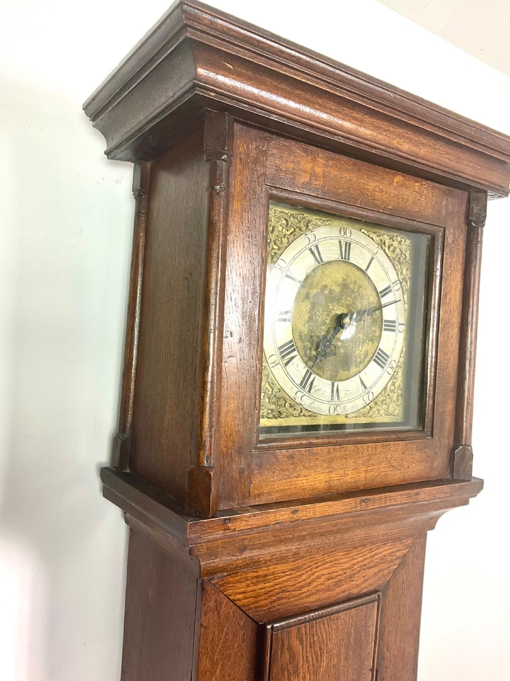 An antique Georgian oak longcase clock hood with a square brass dial, engraved numerals, corner spandrels, and turned side columns.