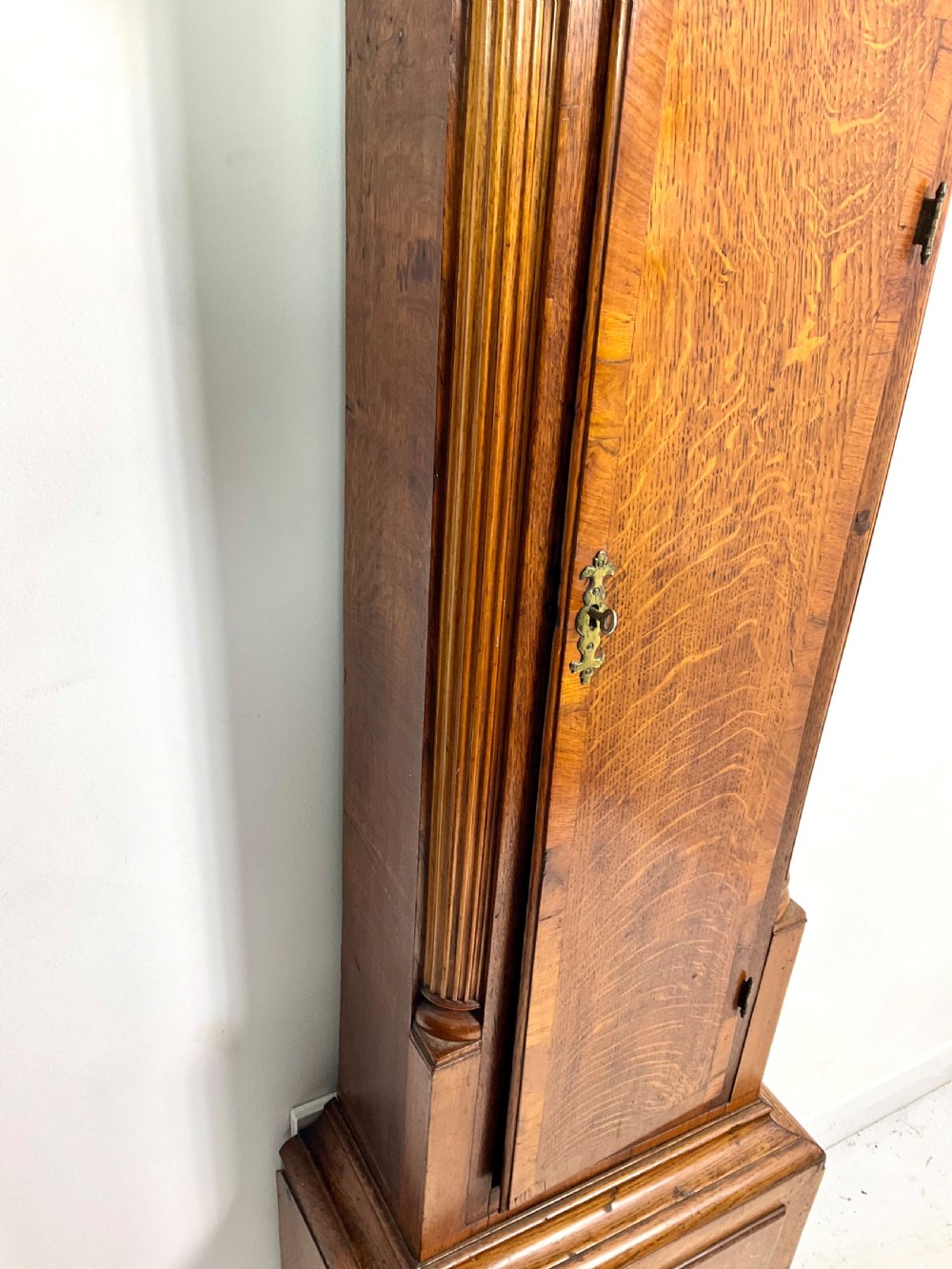 An early Georgian longcase clock featuring a warm oak case with turned hood columns and an engraved brass dial. View II