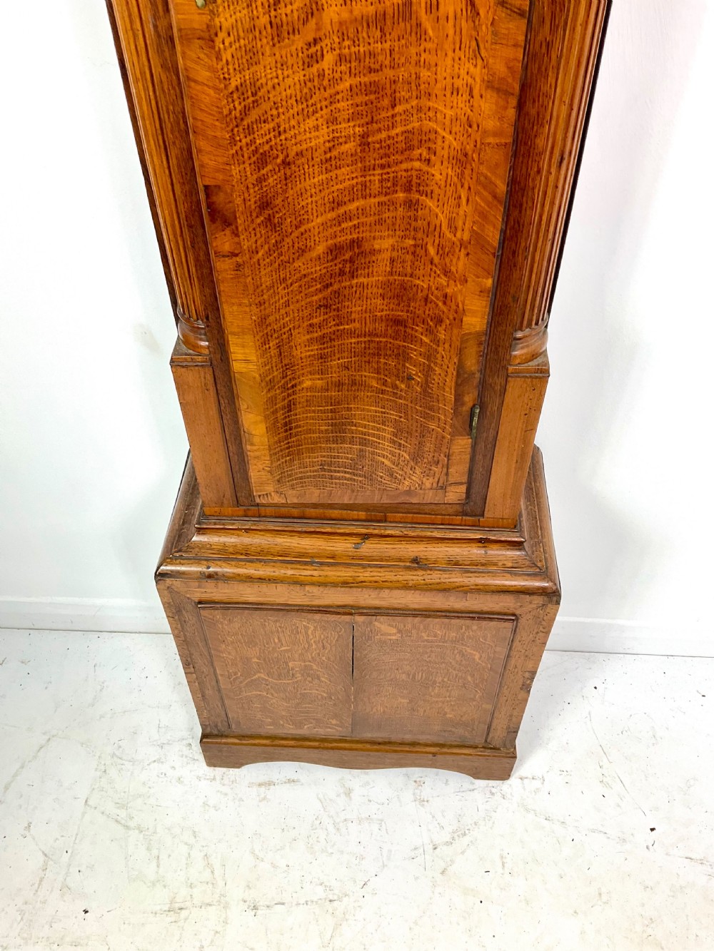 An early Georgian longcase clock featuring a warm oak case with turned hood columns and an engraved brass dial. View VII