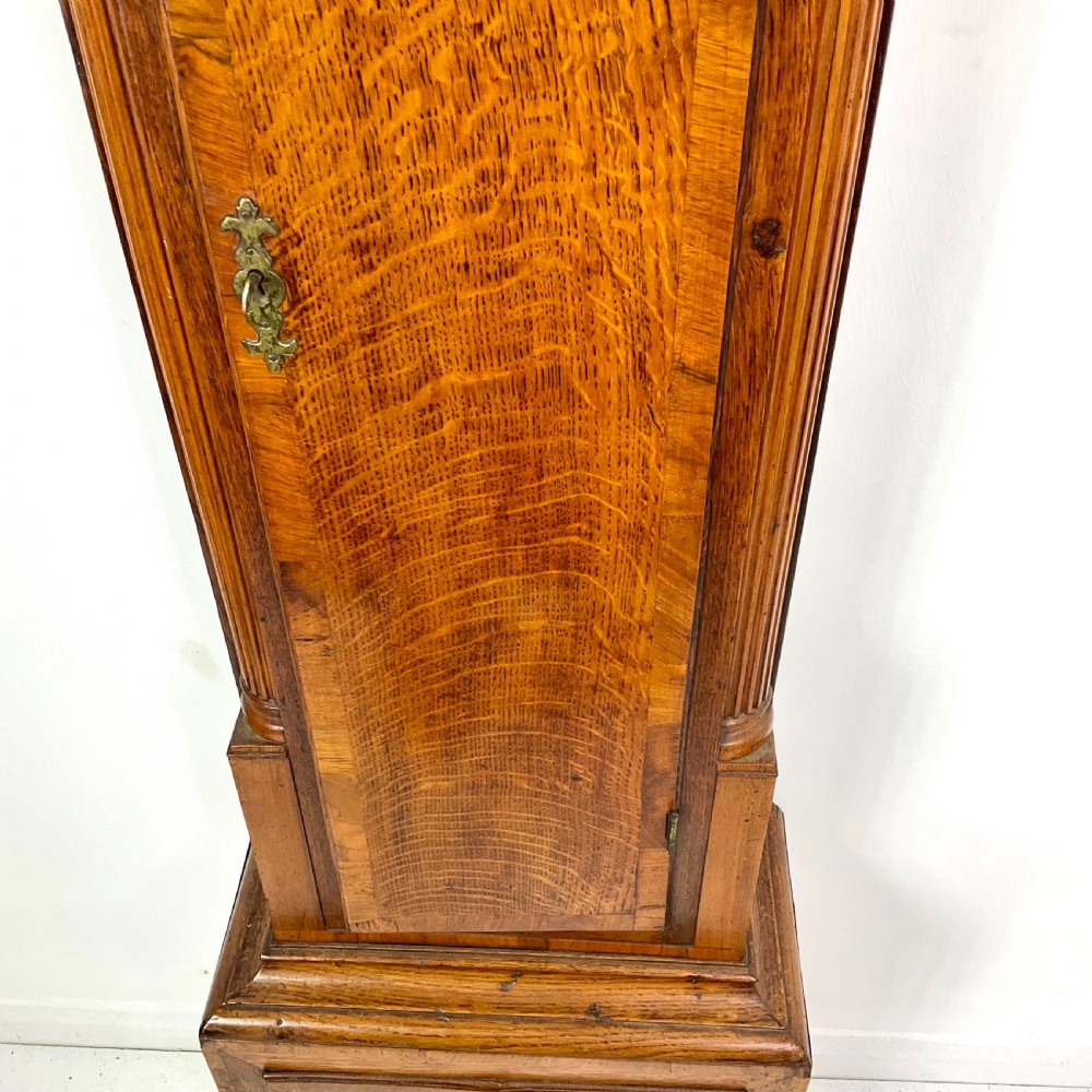 An early Georgian longcase clock featuring a warm oak case with turned hood columns and an engraved brass dial. View VIII