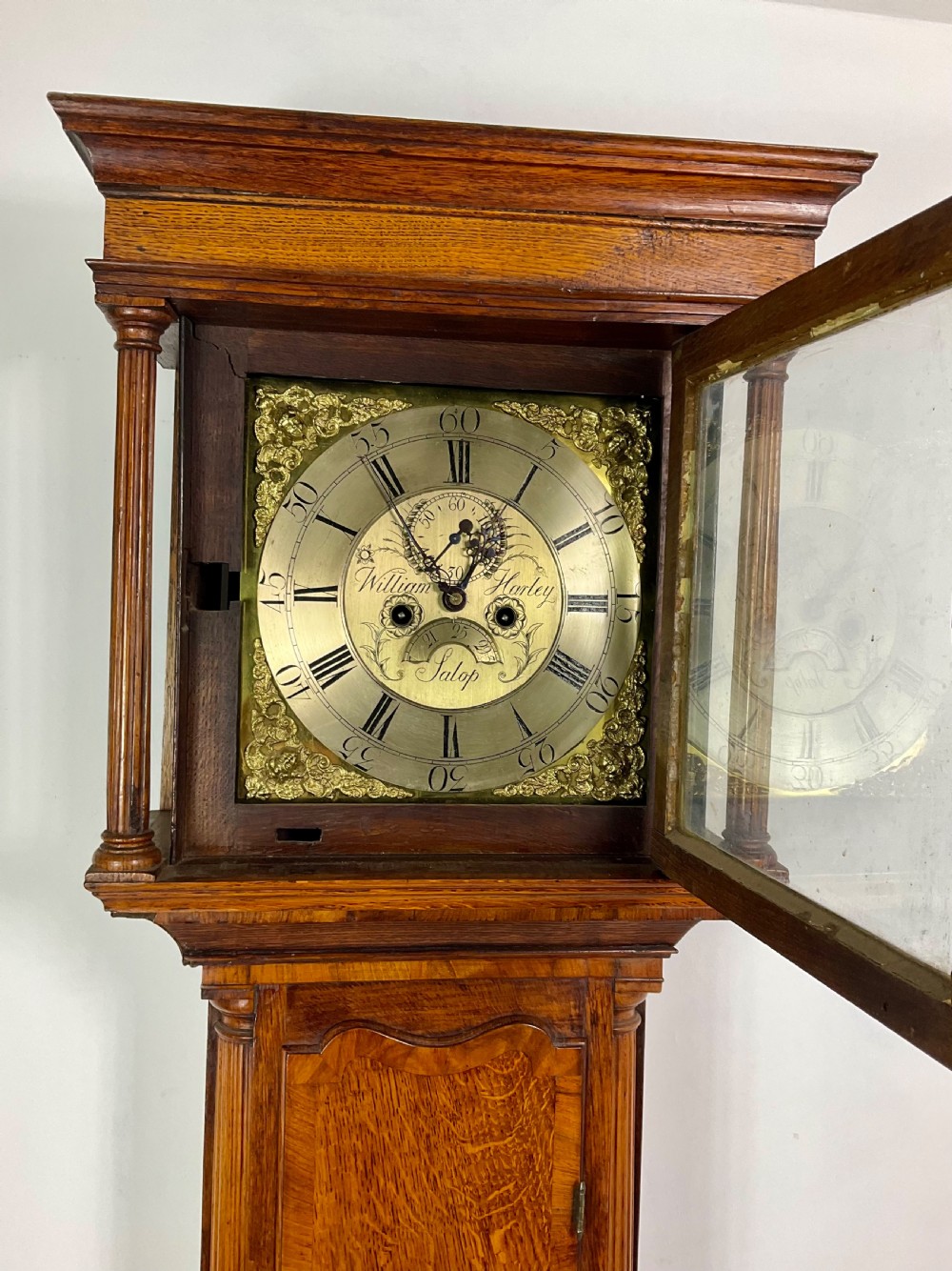 An early Georgian longcase clock featuring a warm oak case with turned hood columns and an engraved brass dial. View XI