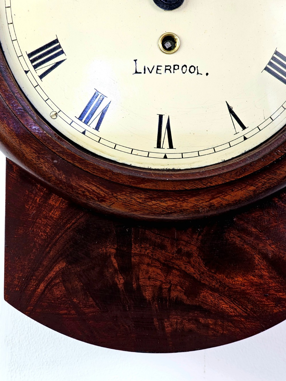 An early Victorian drop dial wall clock featuring a circular off-white dial with Roman numerals, a polished brass bezel, and a rich mahogany casing. View II