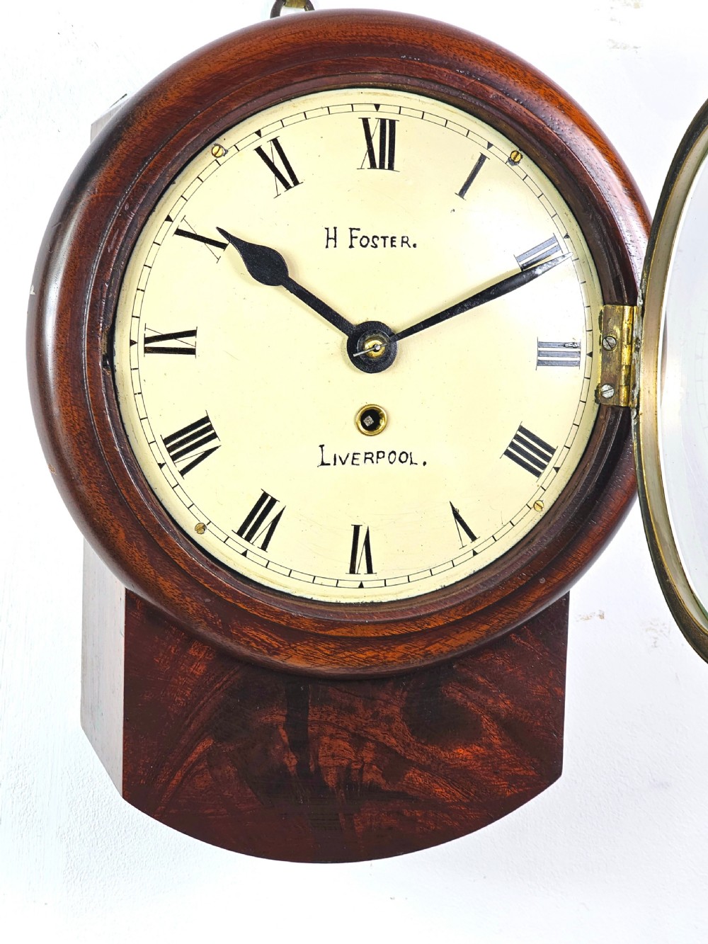 An early Victorian drop dial wall clock featuring a circular off-white dial with Roman numerals, a polished brass bezel, and a rich mahogany casing. View III
