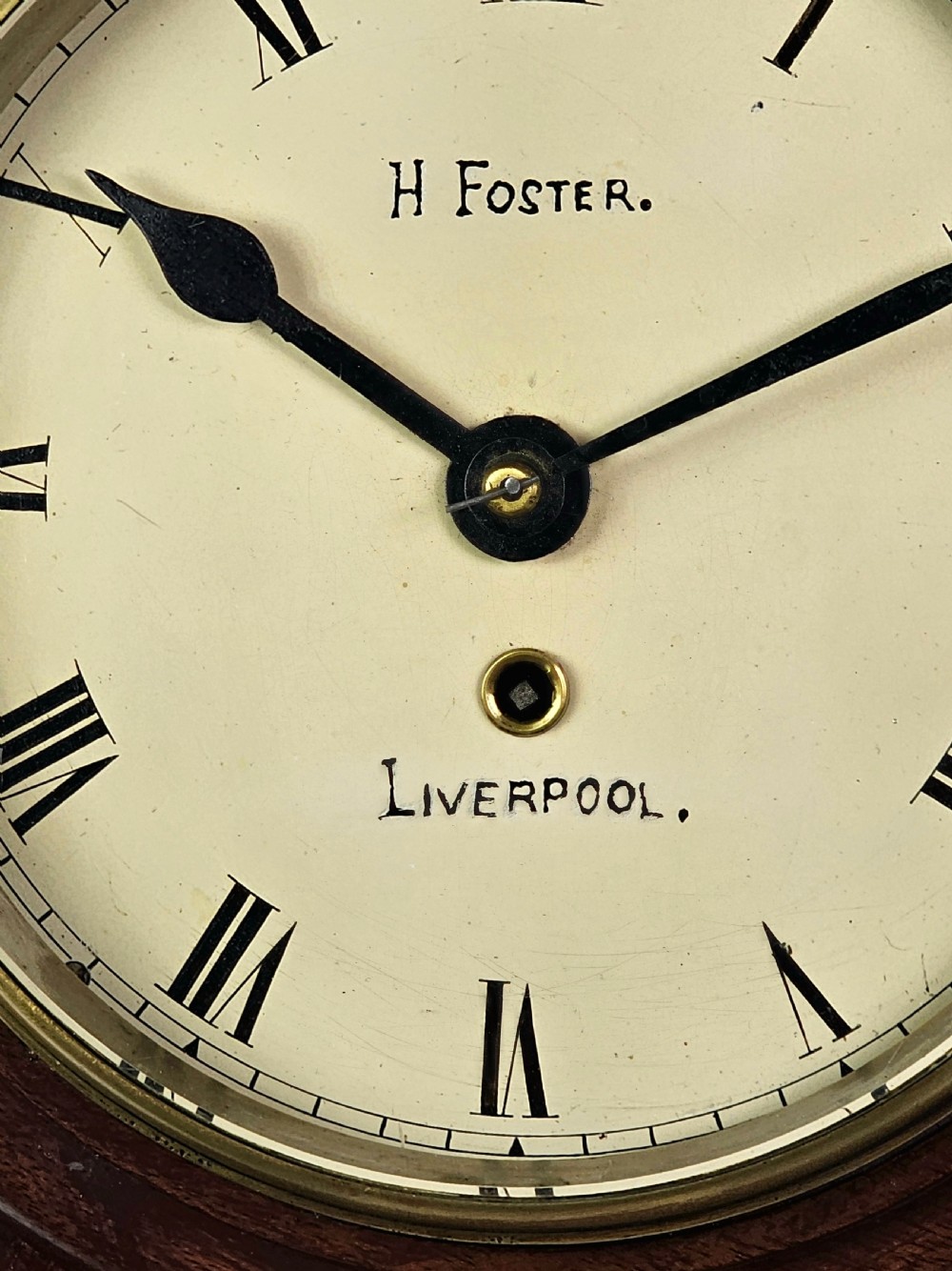 An early Victorian drop dial wall clock featuring a circular off-white dial with Roman numerals, a polished brass bezel, and a rich mahogany casing. View IV