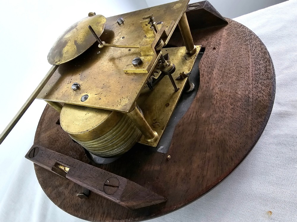 An early Victorian drop dial wall clock featuring a circular off-white dial with Roman numerals, a polished brass bezel, and a rich mahogany casing. View VI