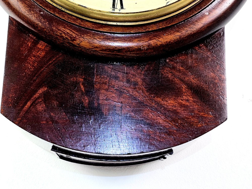 An early Victorian drop dial wall clock featuring a circular off-white dial with Roman numerals, a polished brass bezel, and a rich mahogany casing. View VII