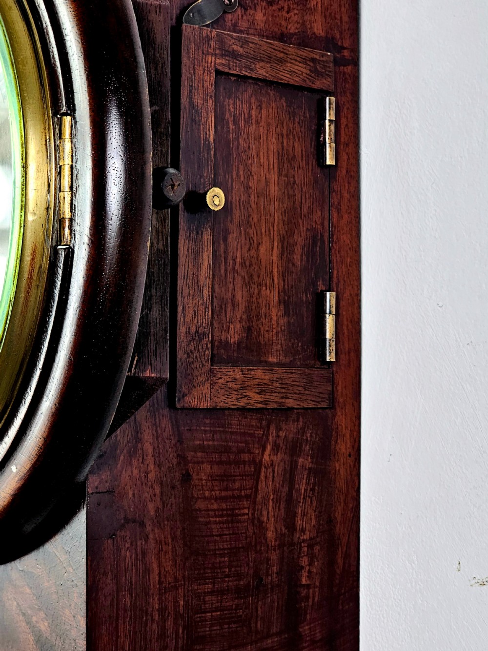 An early Victorian drop dial wall clock featuring a circular off-white dial with Roman numerals, a polished brass bezel, and a rich mahogany casing. View VIII
