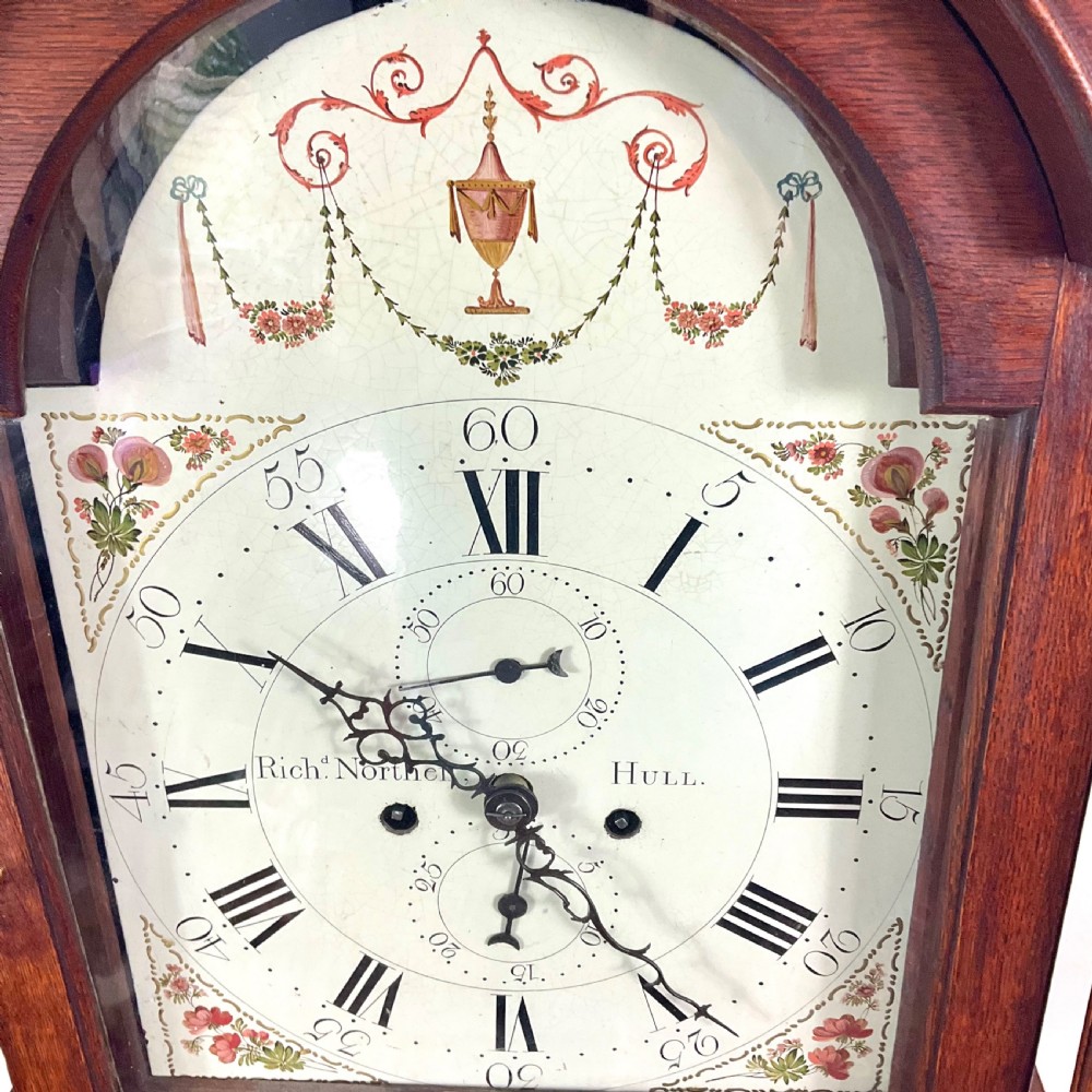 A Georgian oak longcase clock featuring a swan-neck pediment, brass ball finials, fluted columns, and a painted arch dial displaying Roman numerals. View X