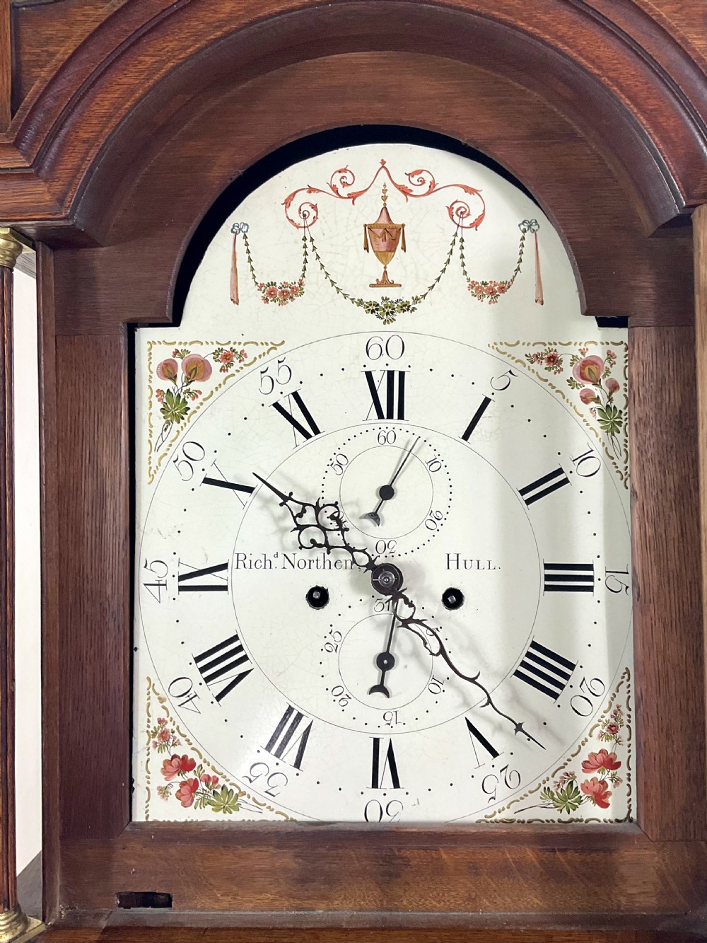 A Georgian oak longcase clock featuring a swan-neck pediment, brass ball finials, fluted columns, and a painted arch dial displaying Roman numerals. View IV