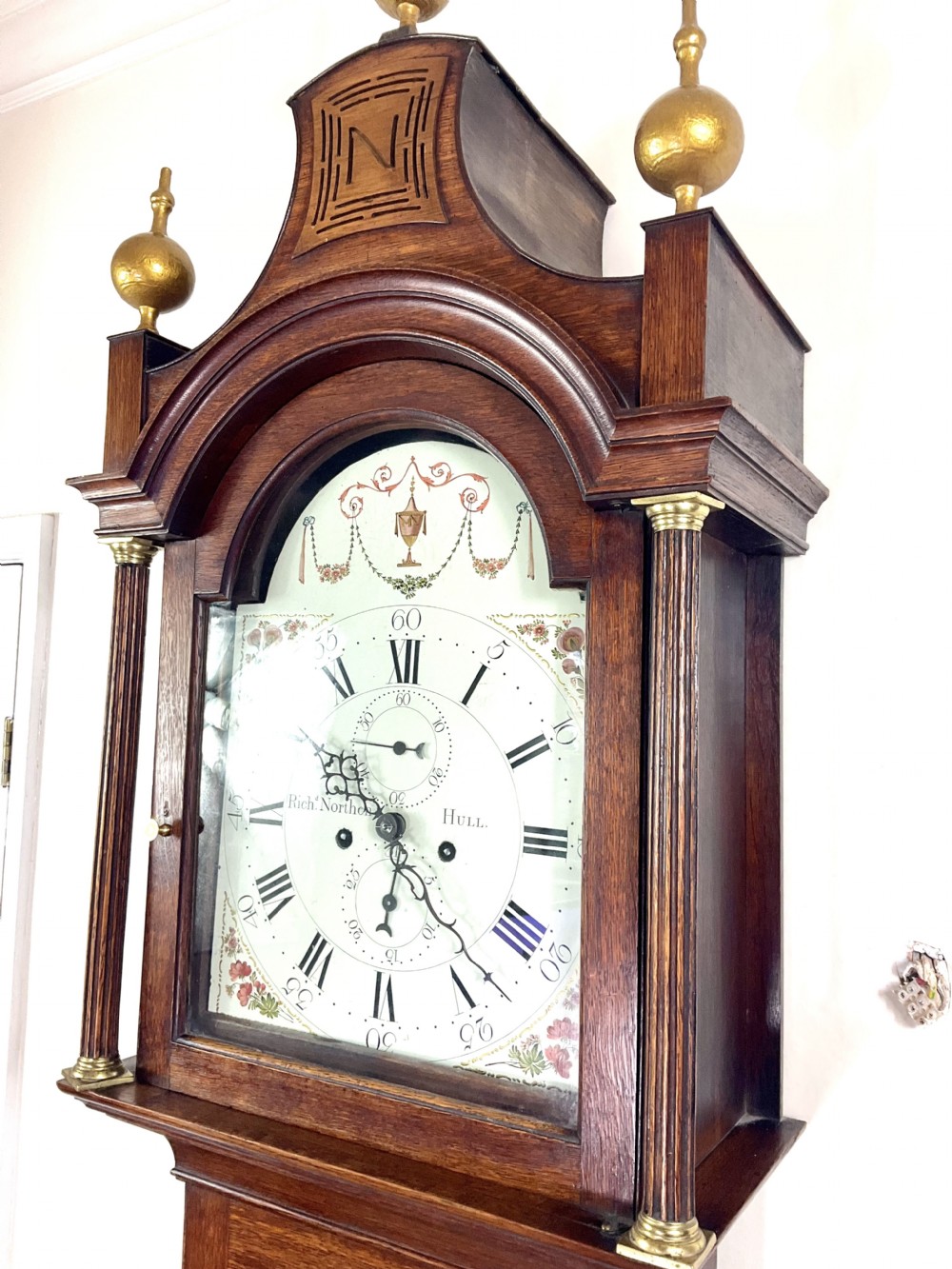A Georgian oak longcase clock featuring a swan-neck pediment, brass ball finials, fluted columns, and a painted arch dial displaying Roman numerals.