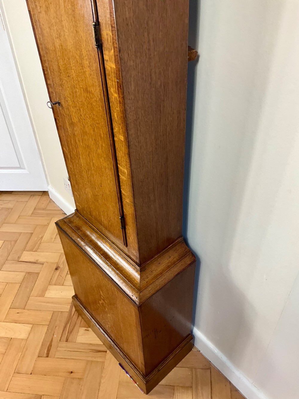 An antique Georgian longcase clock hood crafted from light oak with an arched glass door, brass-capped side columns, and a painted white dial with Roman numerals. View III