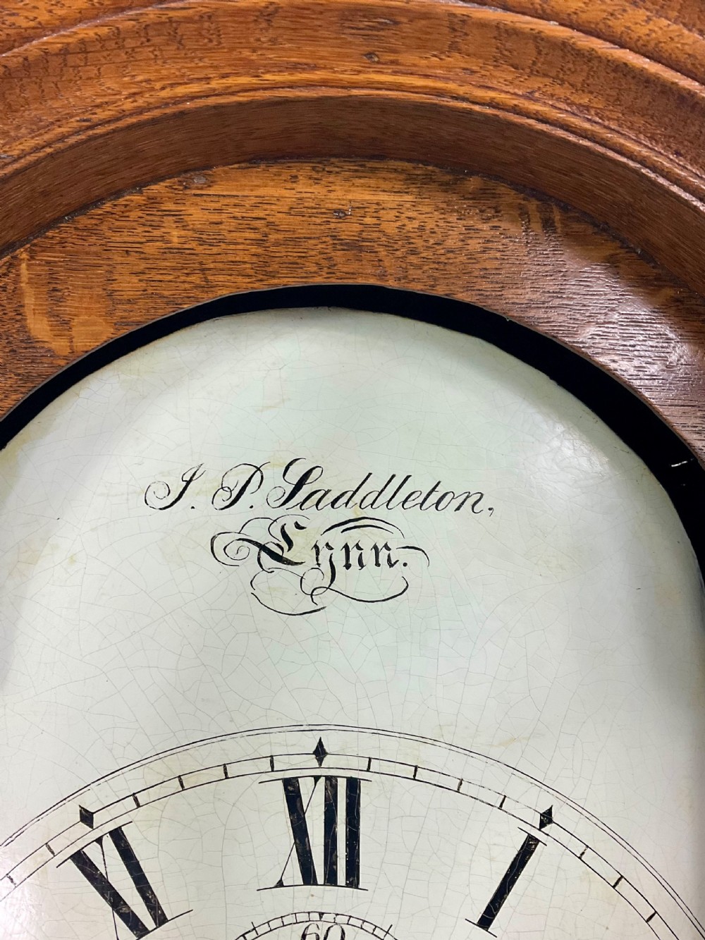 An antique Georgian longcase clock hood crafted from light oak with an arched glass door, brass-capped side columns, and a painted white dial with Roman numerals. View IV