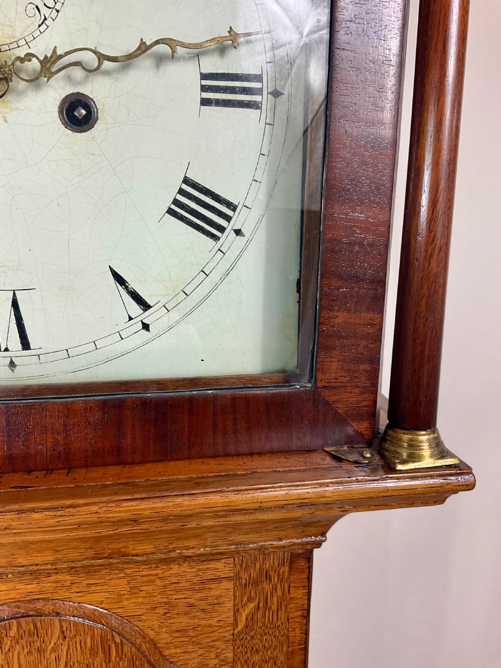 An antique Georgian longcase clock hood crafted from light oak with an arched glass door, brass-capped side columns, and a painted white dial with Roman numerals. View IX