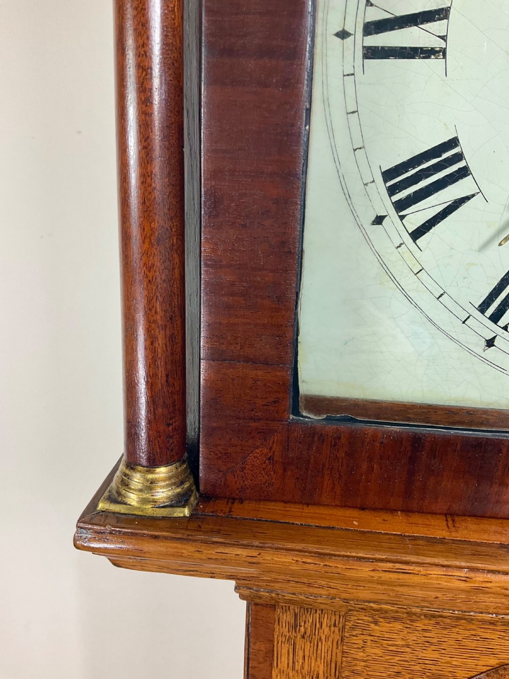 An antique Georgian longcase clock hood crafted from light oak with an arched glass door, brass-capped side columns, and a painted white dial with Roman numerals. View X