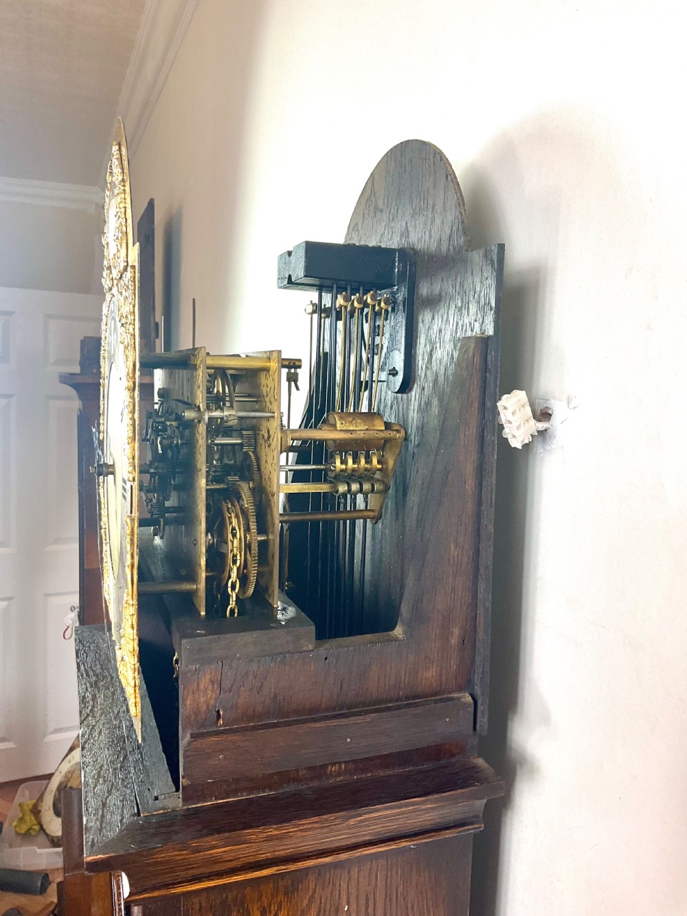 A dark oak grandmother longcase clock featuring an arched hood, clear glass door, and a brass dial with Roman numerals. View IX