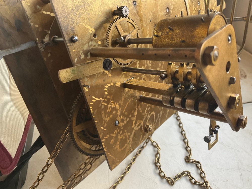 A dark oak grandmother longcase clock featuring an arched hood, clear glass door, and a brass dial with Roman numerals. View XI