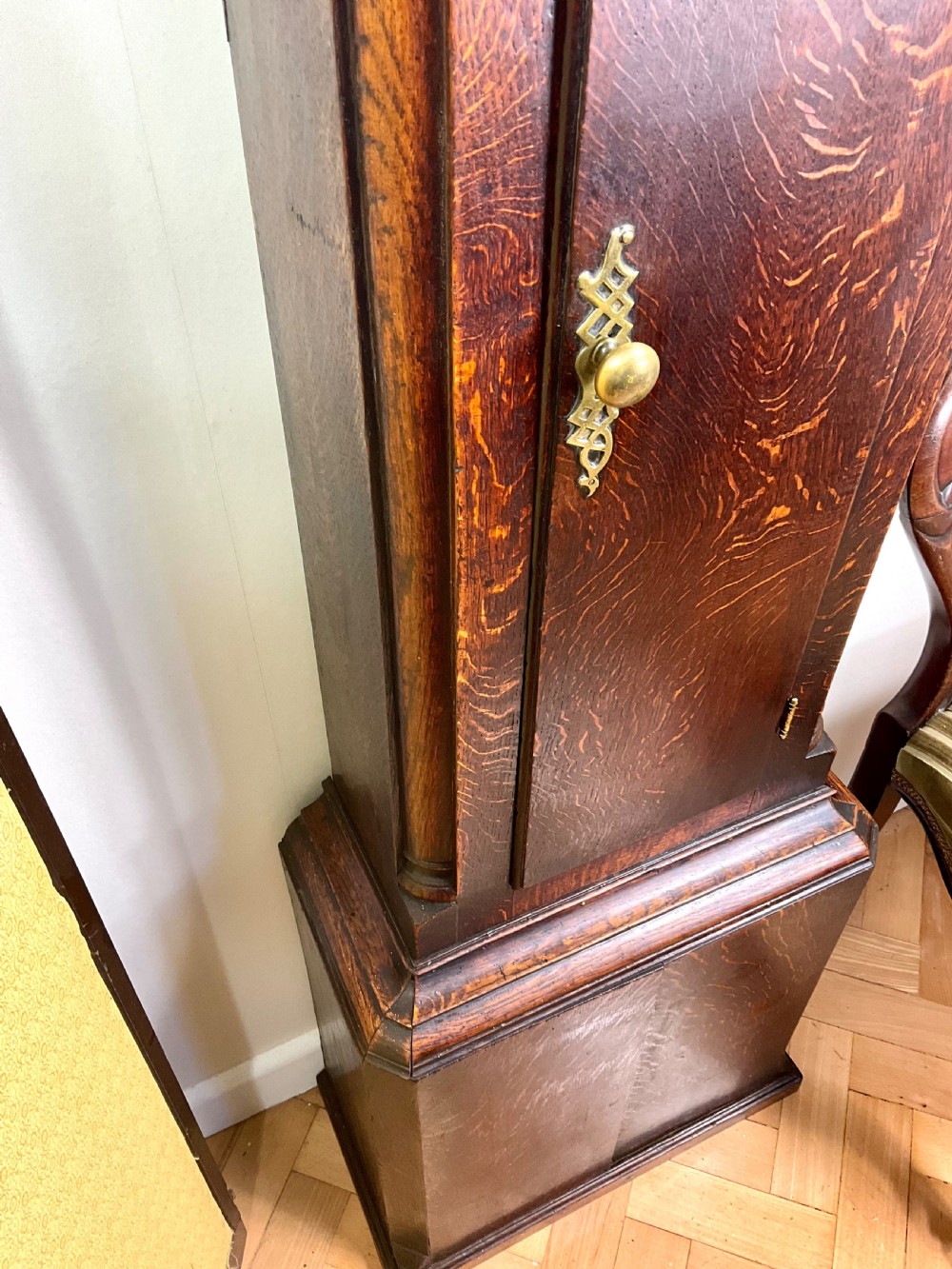 An Early Georgian longcase clock constructed from dark oak featuring a square hood, brass dial with Roman numerals, and an arched trunk door. View II