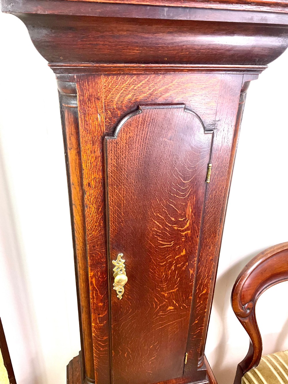 An Early Georgian longcase clock constructed from dark oak featuring a square hood, brass dial with Roman numerals, and an arched trunk door. View III