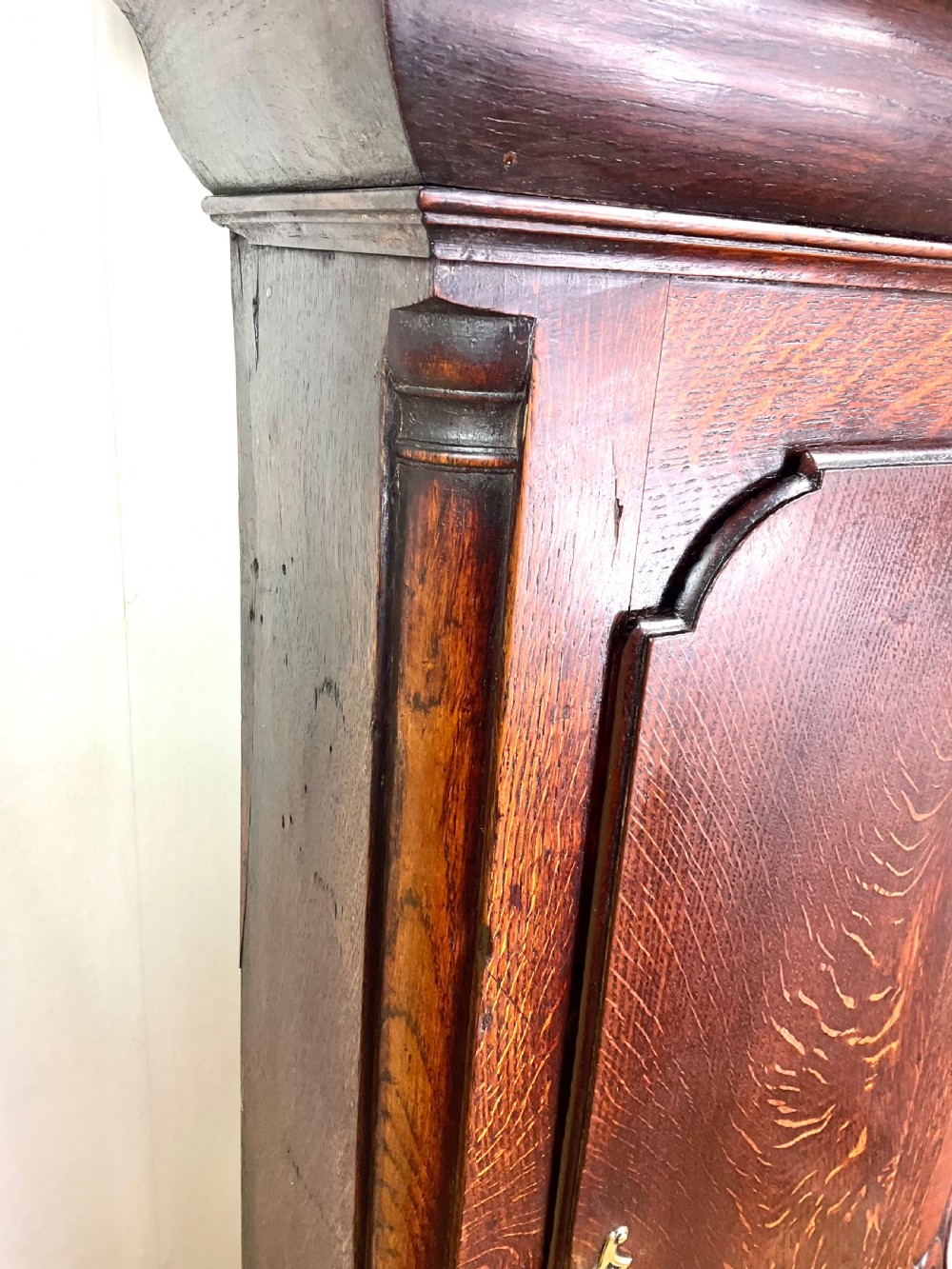An Early Georgian longcase clock constructed from dark oak featuring a square hood, brass dial with Roman numerals, and an arched trunk door. View VI