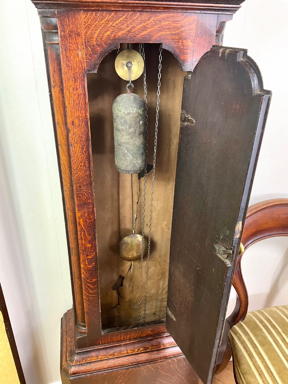 An Early Georgian longcase clock constructed from dark oak featuring a square hood, brass dial with Roman numerals, and an arched trunk door. View VII