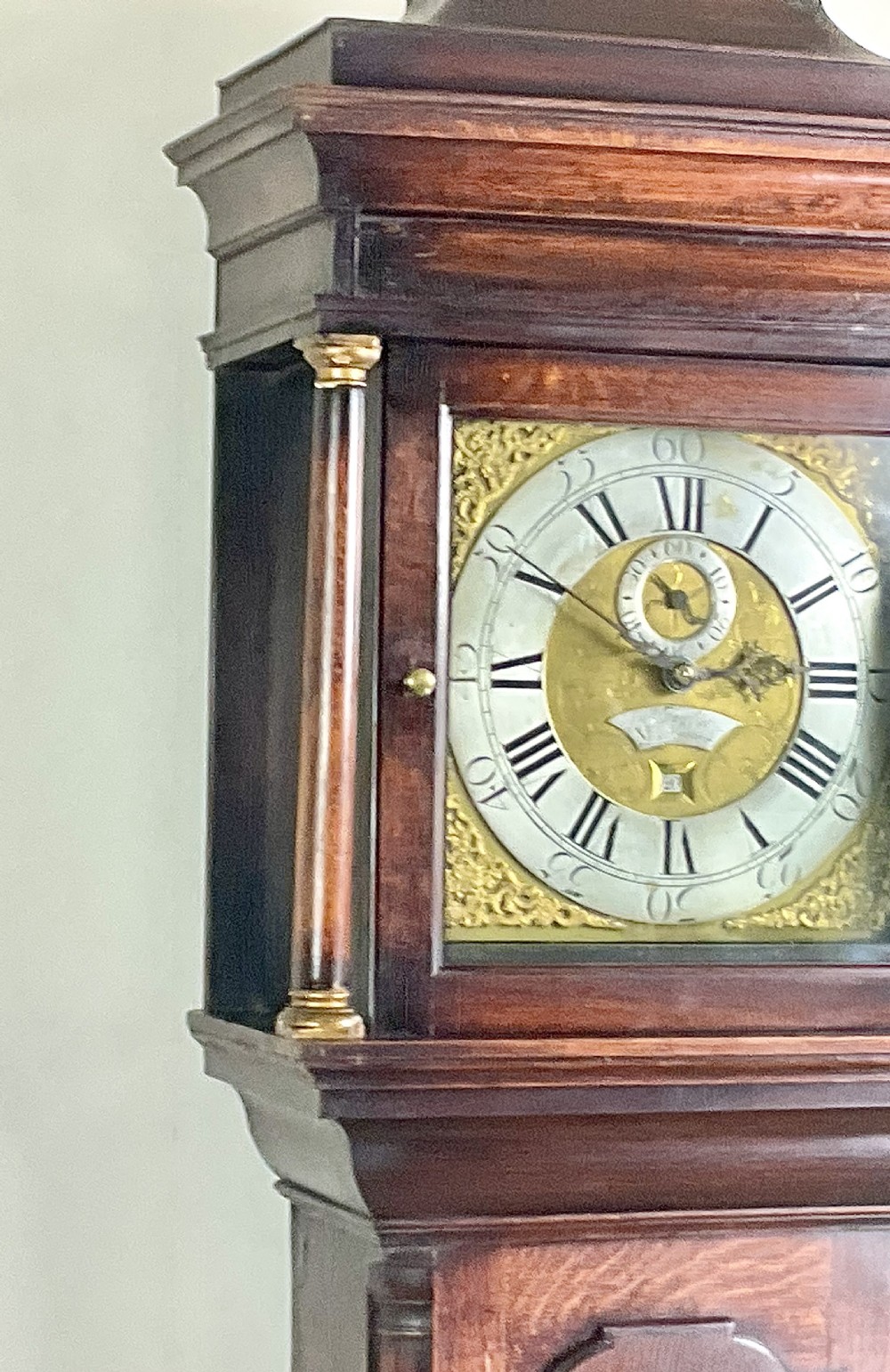 An Early Georgian longcase clock constructed from dark oak featuring a square hood, brass dial with Roman numerals, and an arched trunk door. View IX