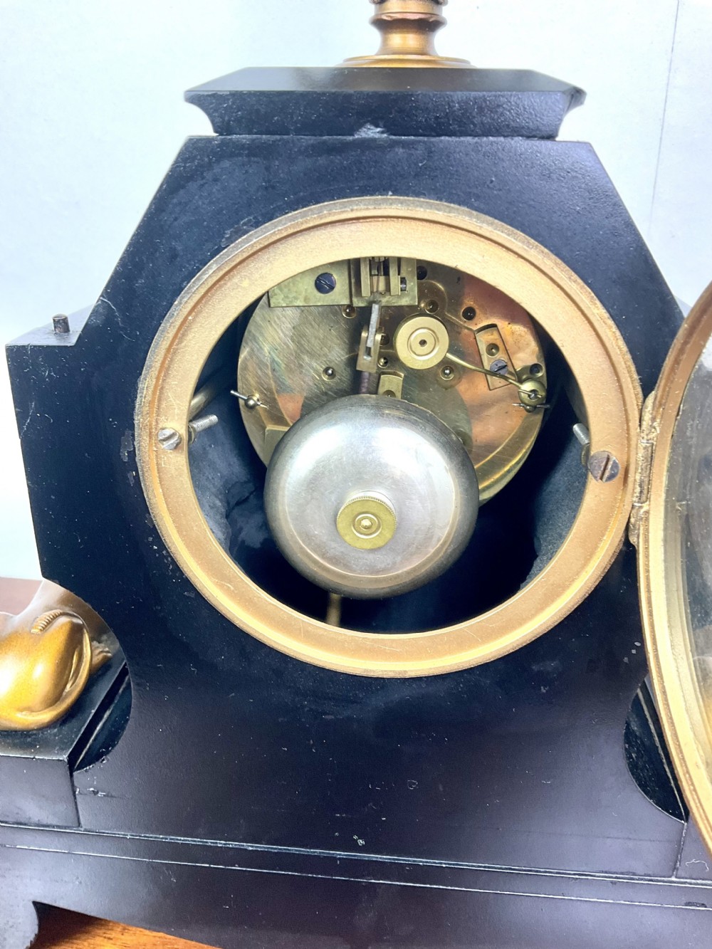 A black slate Egyptian Revival mantel clock featuring a central dial with red Roman numerals, flanked by two gilt bronze sphinxes and topped with a gilt urn finial. View XII