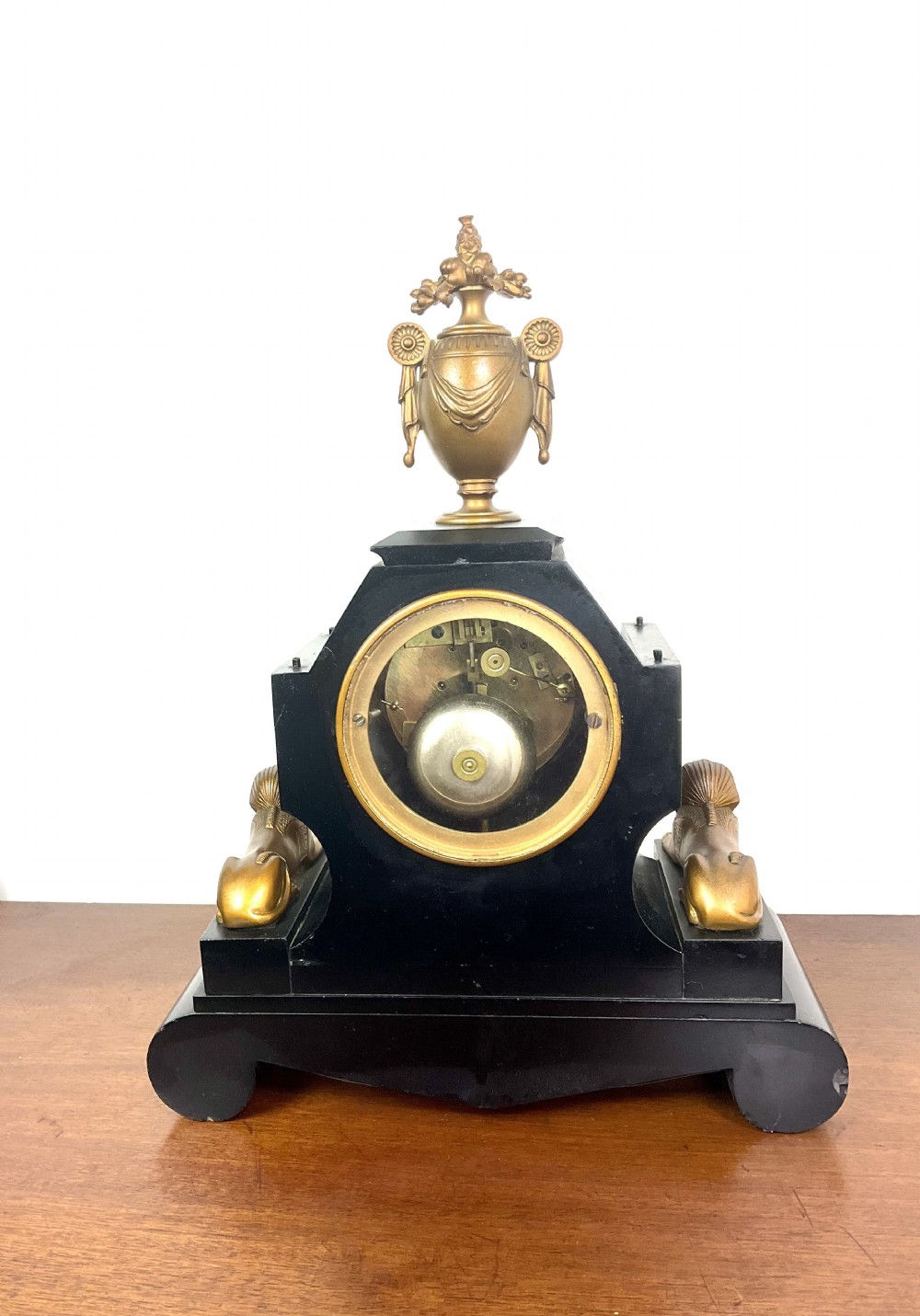 A black slate Egyptian Revival mantel clock featuring a central dial with red Roman numerals, flanked by two gilt bronze sphinxes and topped with a gilt urn finial. View XIII