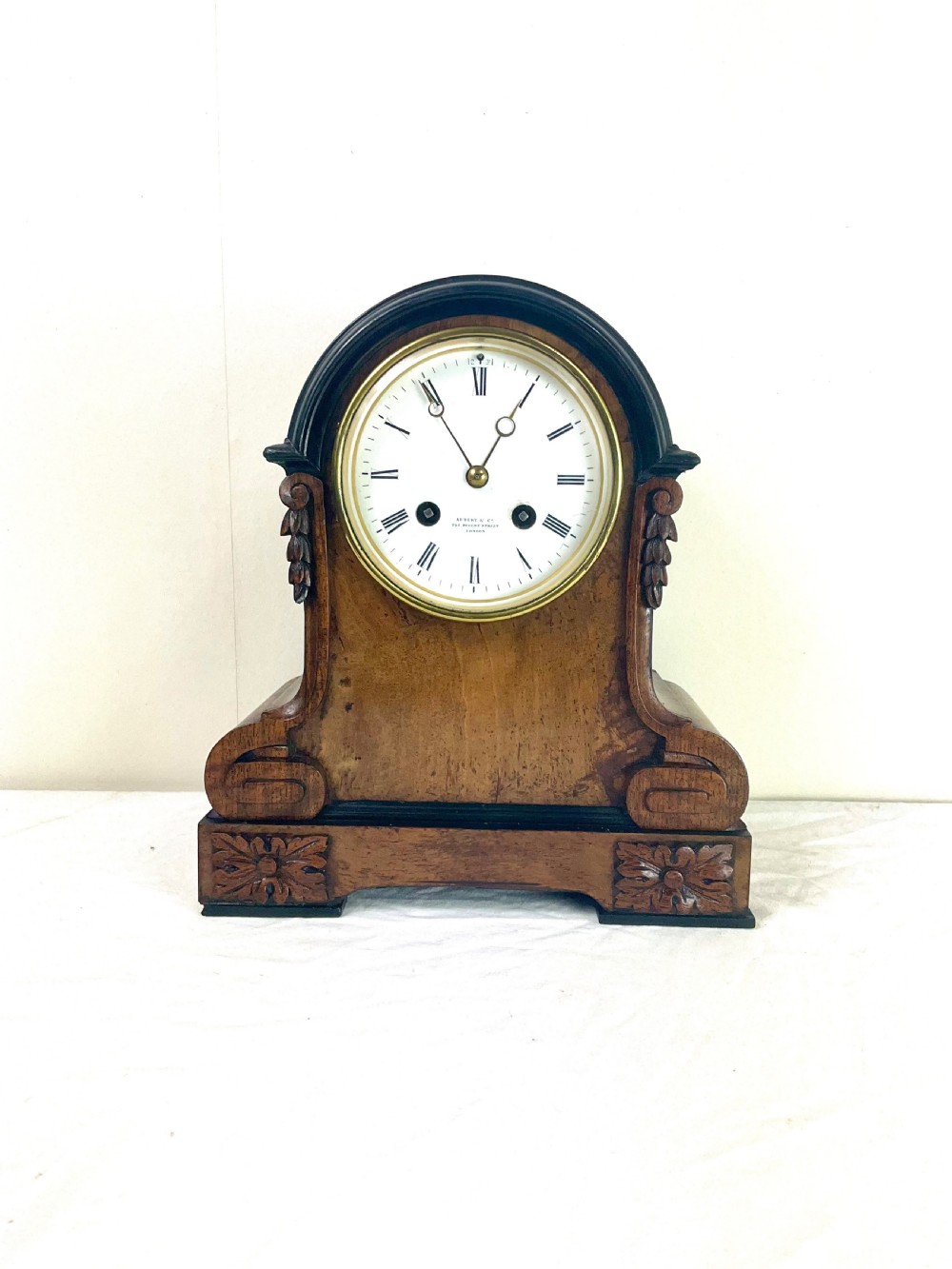 A late 19th-century French mantel clock made of figured walnut with a curved arch top, carved rosettes, and a round white enamel dial.