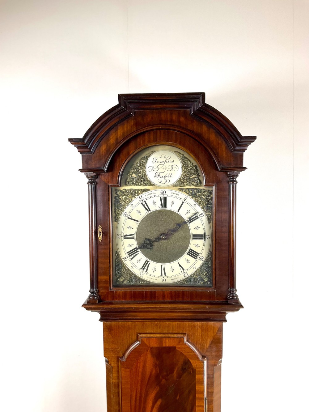 An antique mahogany longcase clock featuring a flame mahogany trunk door, arched hood, and brass dial with Roman numerals. View II