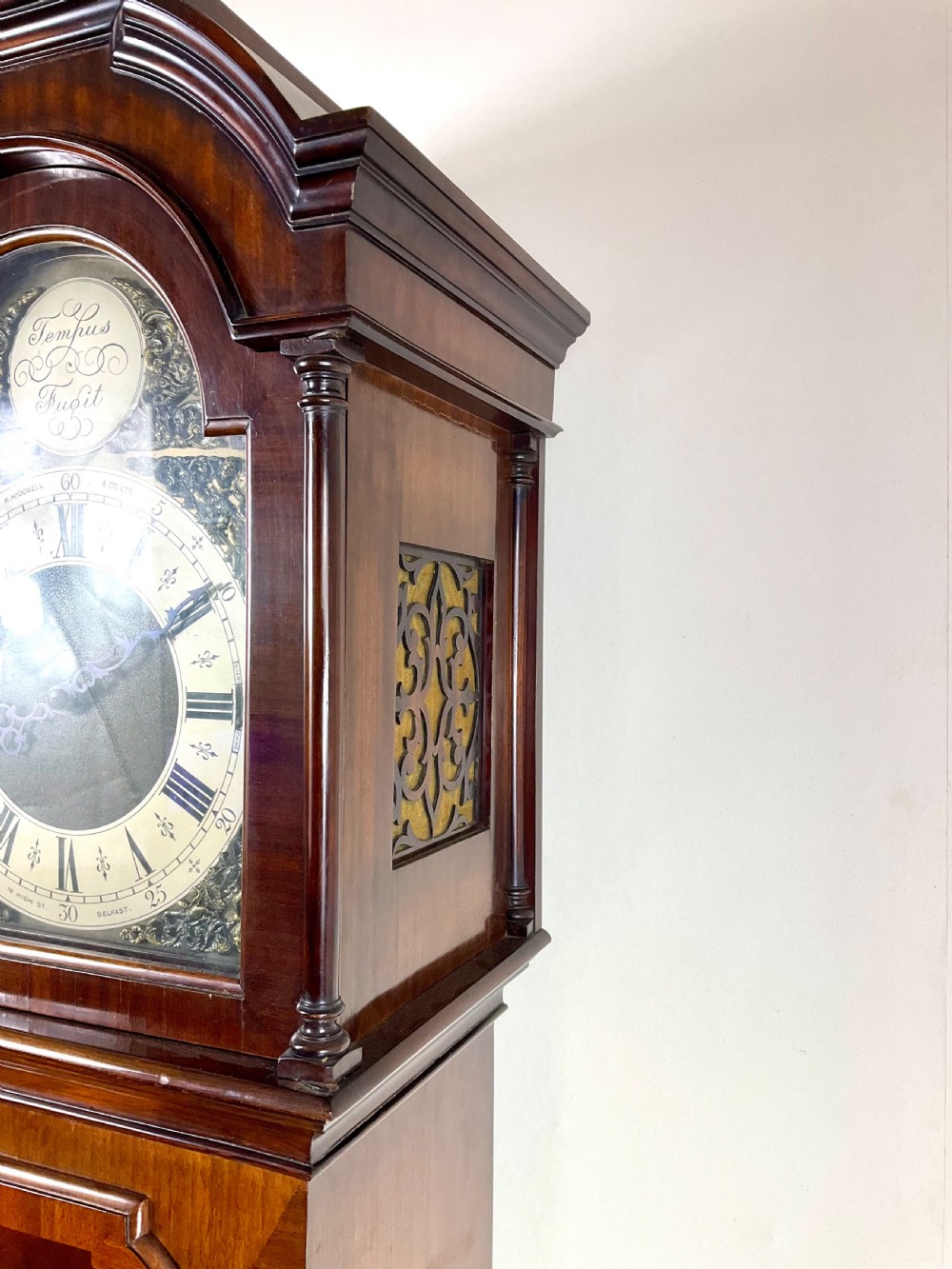 An antique mahogany longcase clock featuring a flame mahogany trunk door, arched hood, and brass dial with Roman numerals. View IV