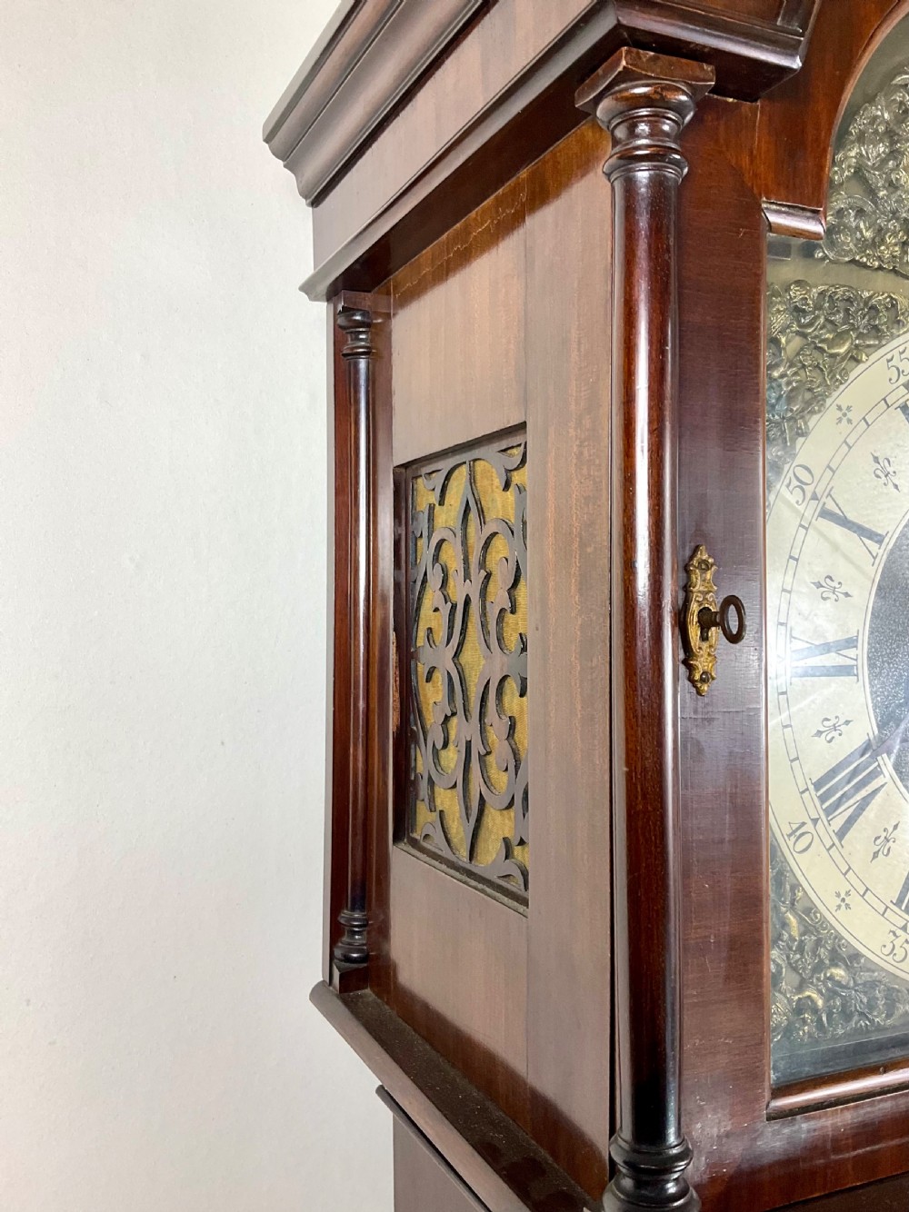An antique mahogany longcase clock featuring a flame mahogany trunk door, arched hood, and brass dial with Roman numerals. View V