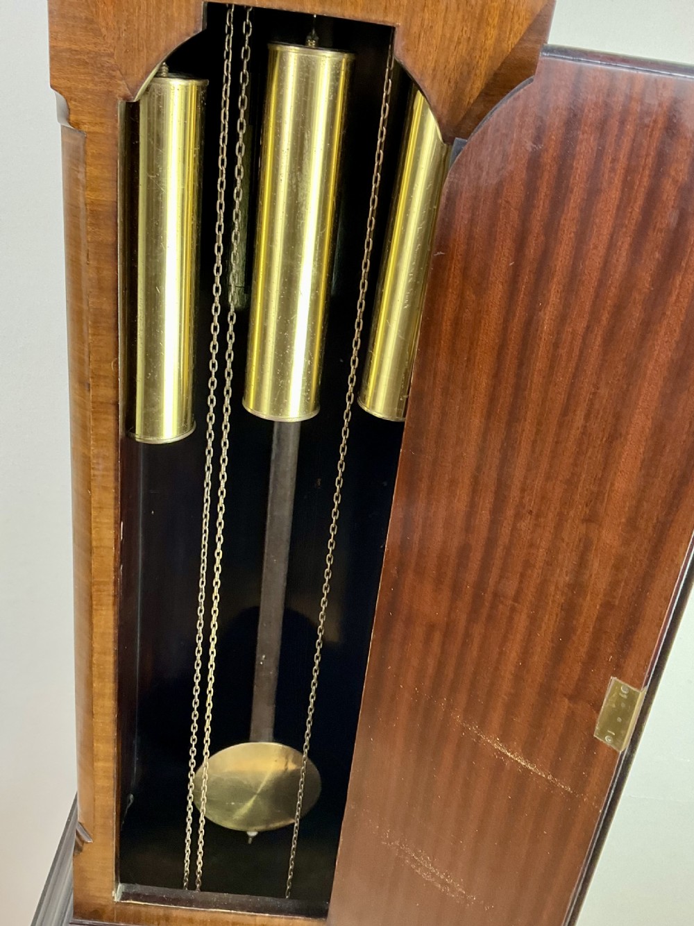 An antique mahogany longcase clock featuring a flame mahogany trunk door, arched hood, and brass dial with Roman numerals. View VI