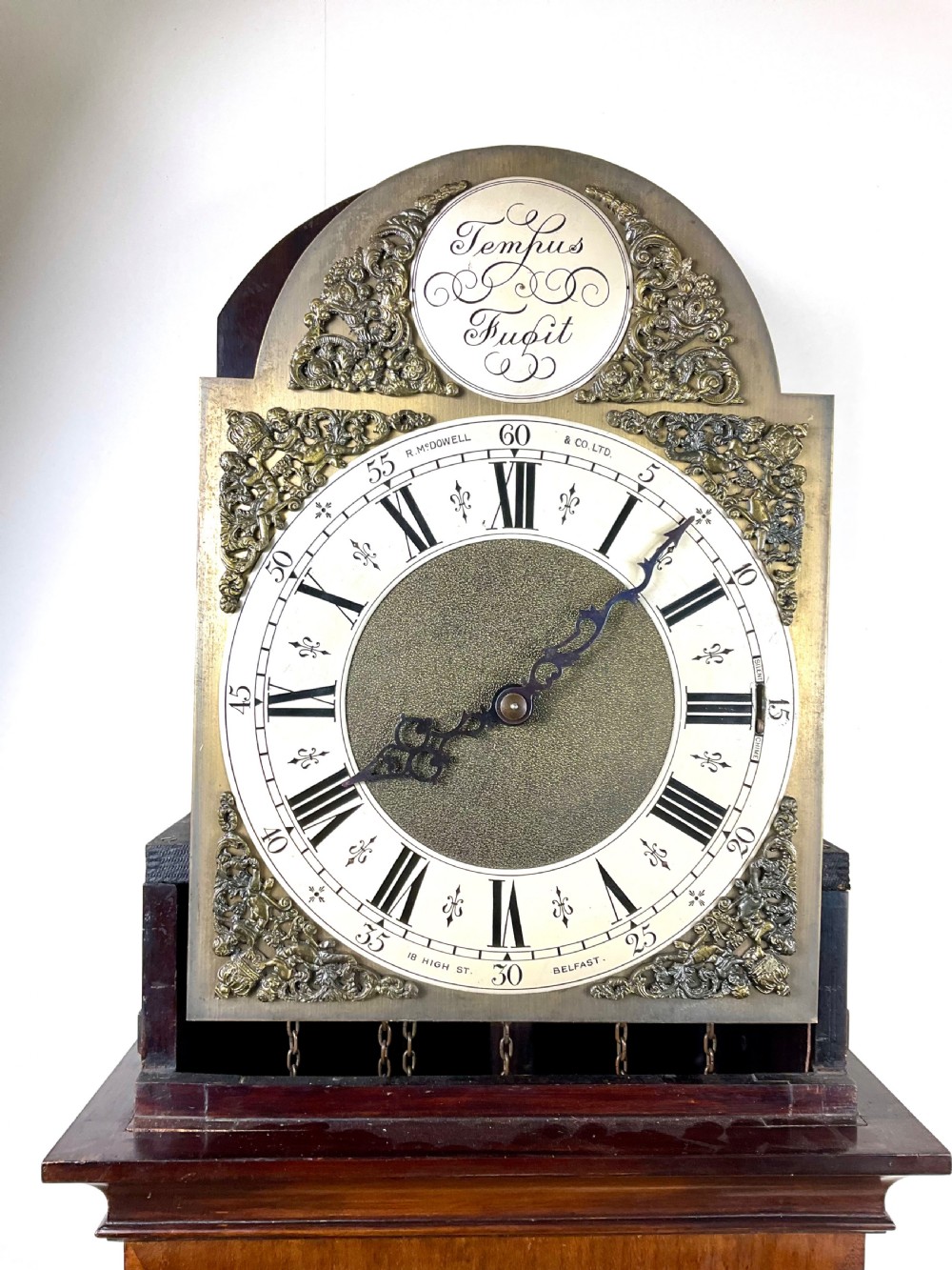 An antique mahogany longcase clock featuring a flame mahogany trunk door, arched hood, and brass dial with Roman numerals. View VIII