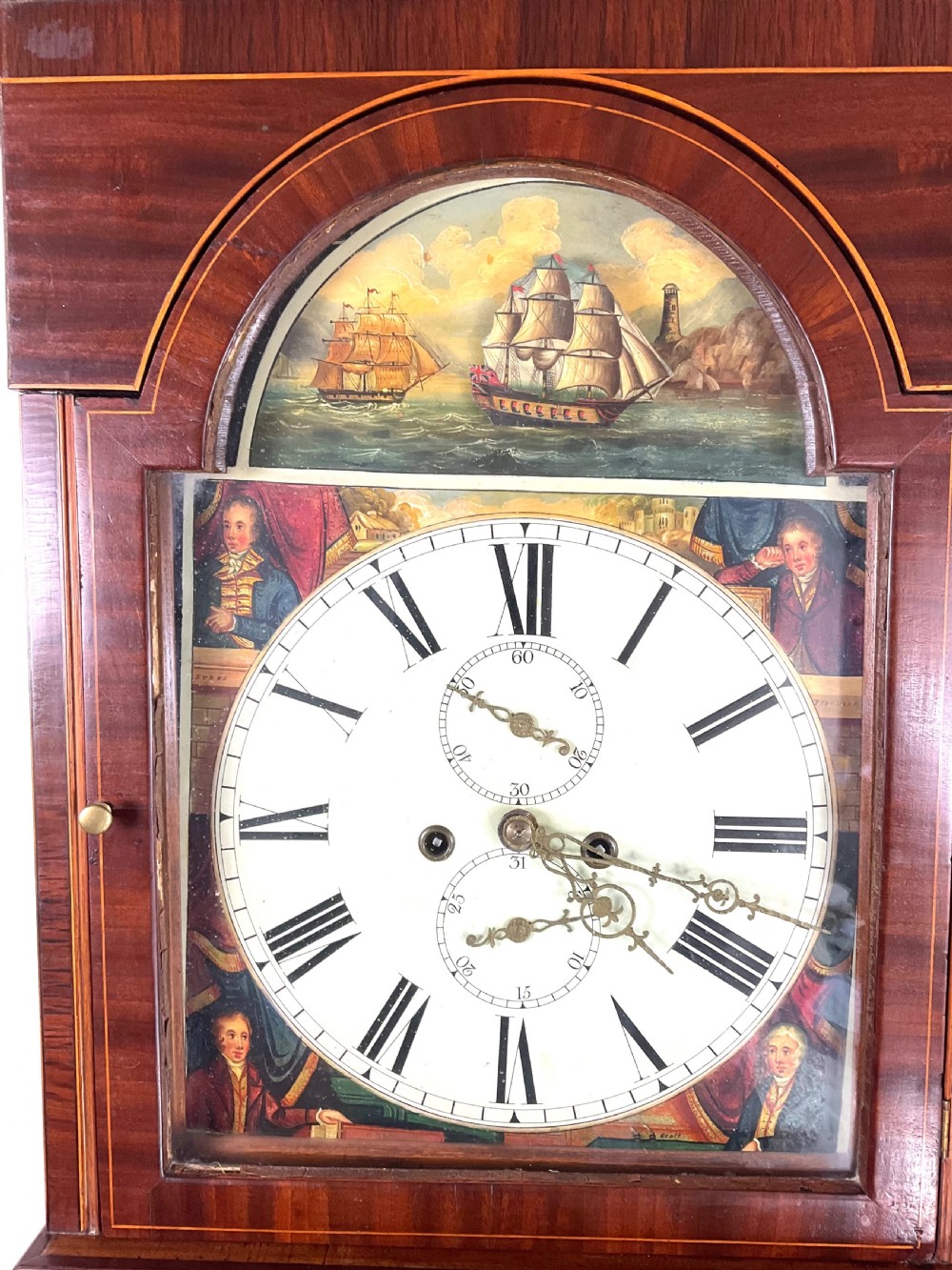 An upper hood section of a Georgian mahogany longcase clock featuring open fretwork pediments, brass finials, and a painted arch dial displaying a rocking ship automaton. View VI