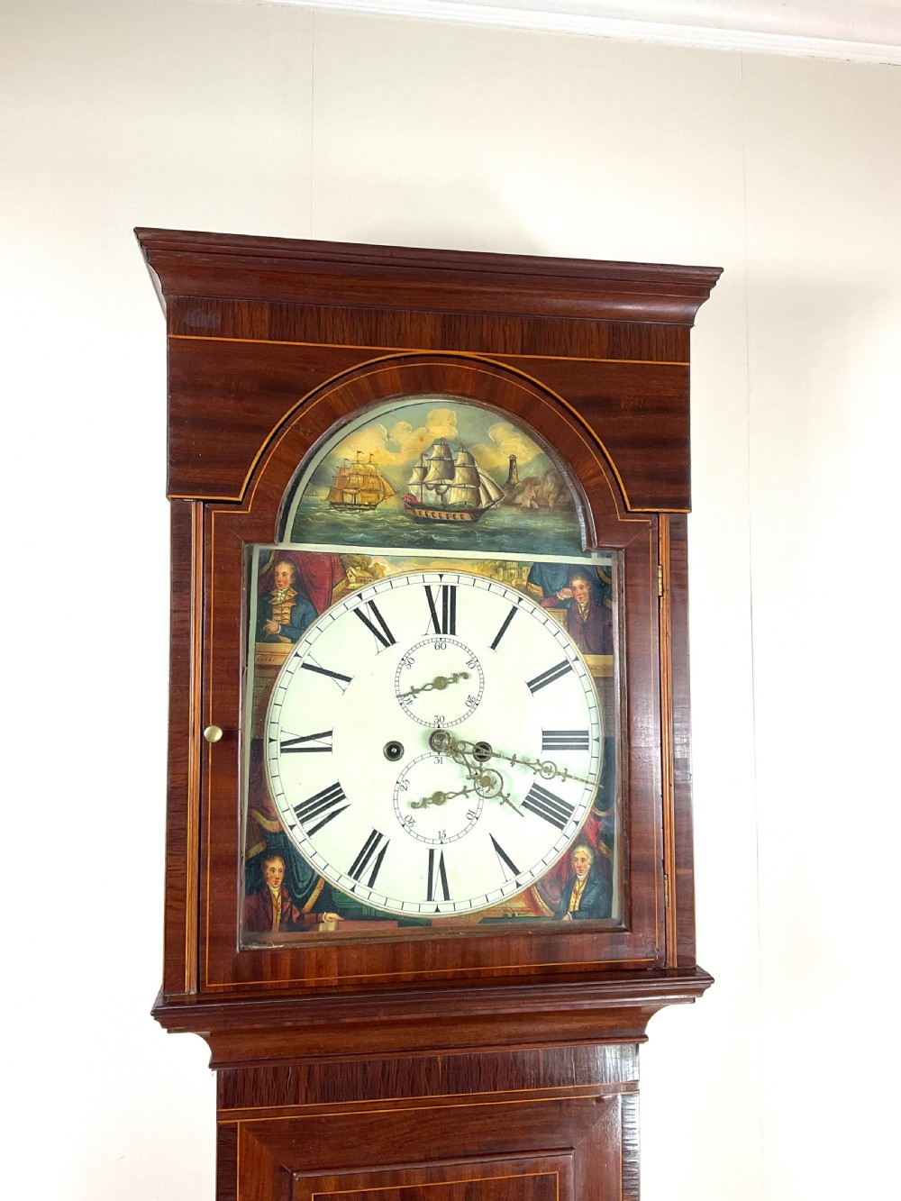 An upper hood section of a Georgian mahogany longcase clock featuring open fretwork pediments, brass finials, and a painted arch dial displaying a rocking ship automaton. View VII