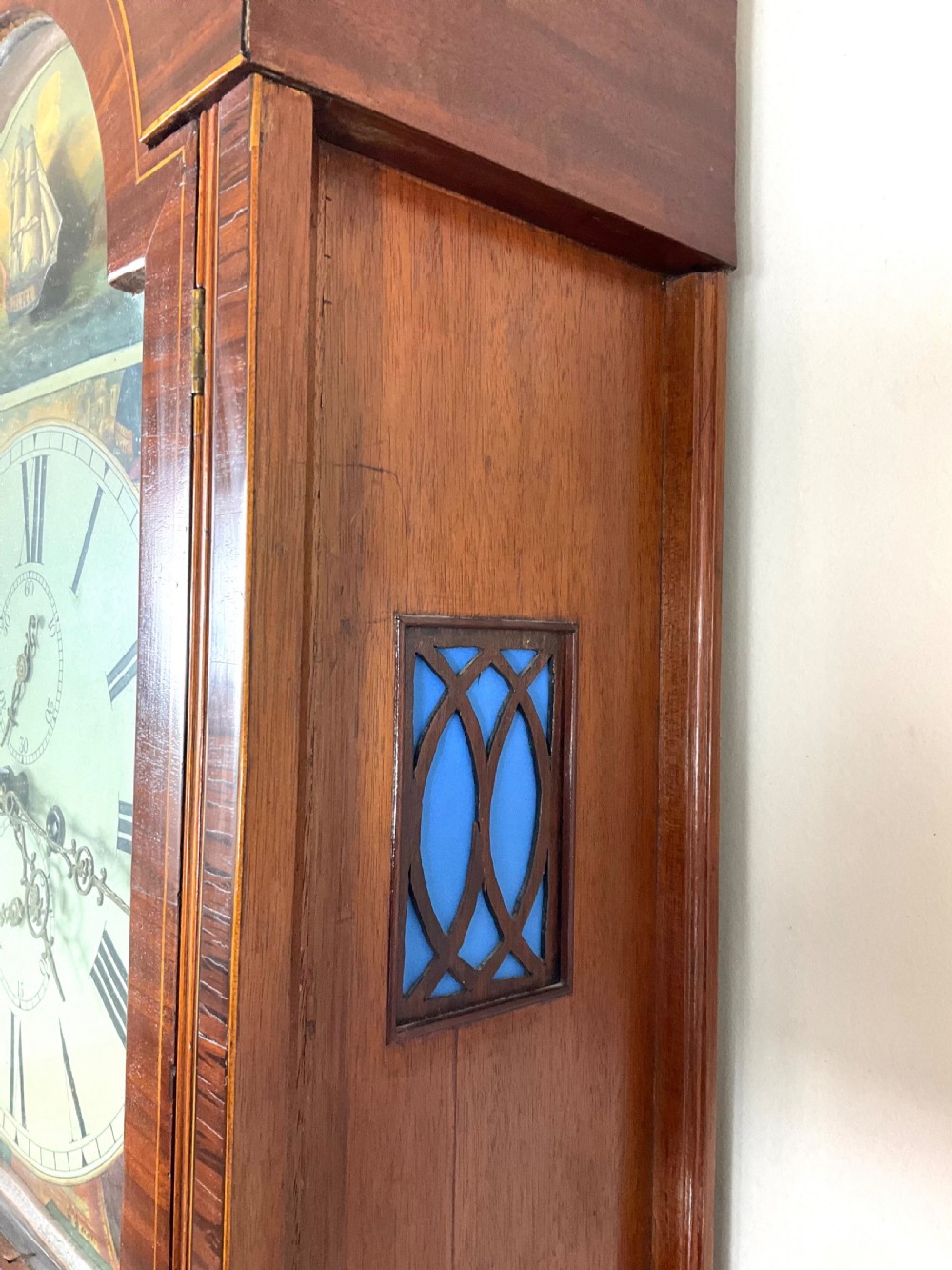 An upper hood section of a Georgian mahogany longcase clock featuring open fretwork pediments, brass finials, and a painted arch dial displaying a rocking ship automaton. View VIII
