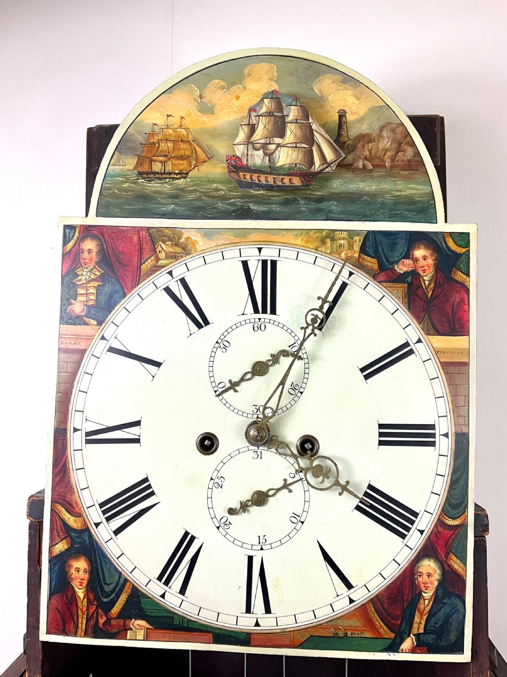 An upper hood section of a Georgian mahogany longcase clock featuring open fretwork pediments, brass finials, and a painted arch dial displaying a rocking ship automaton. View XI