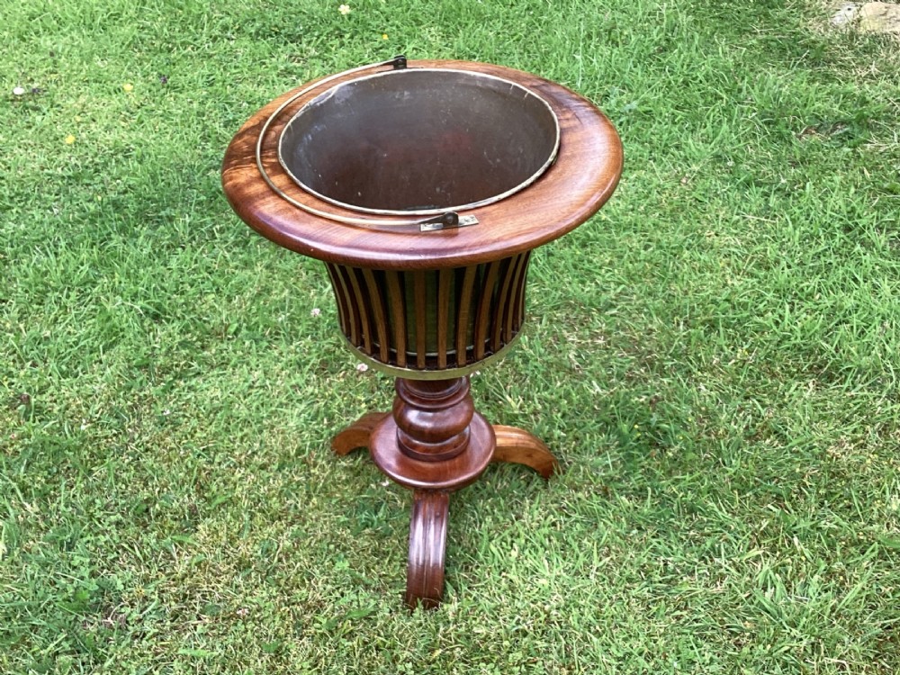 An Edwardian mahogany jardiniere planter featuring a slatted wooden body, turned pedestal base, and a brass-handled metal liner. View II