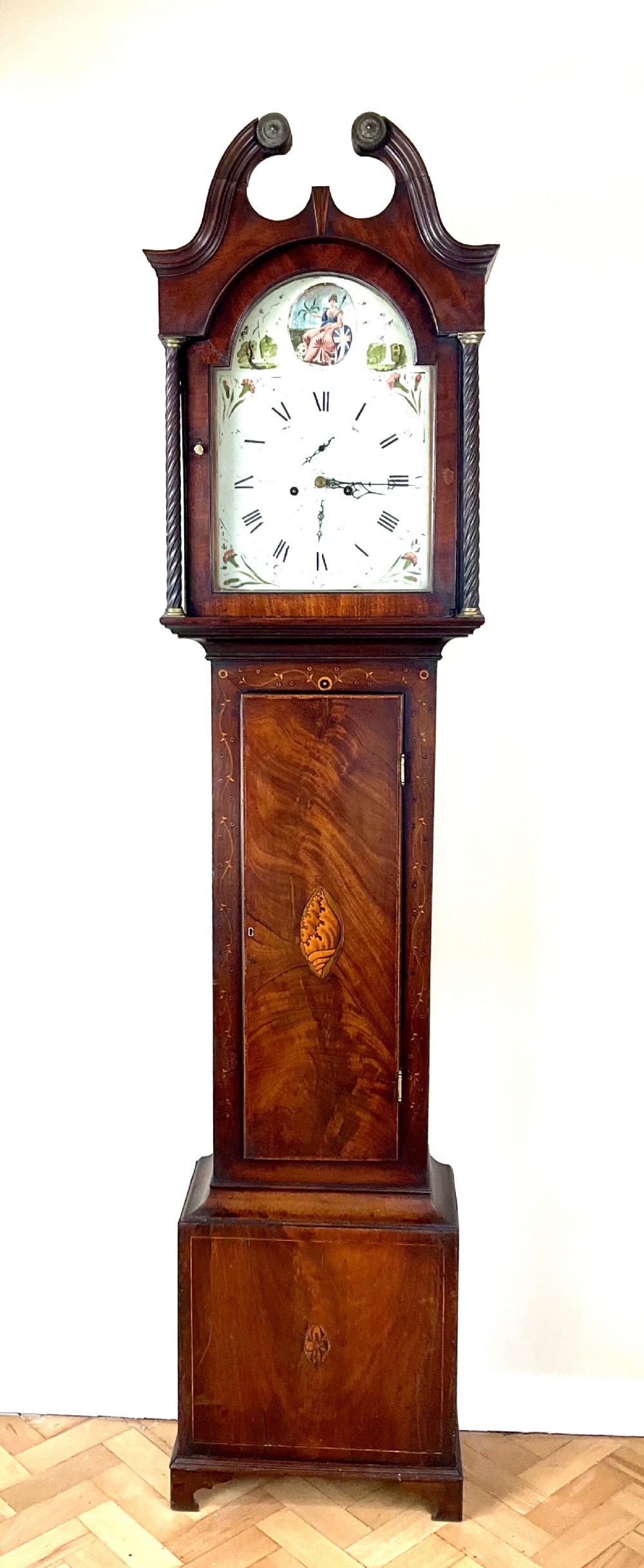 A Georgian mahogany longcase clock featuring a swan-neck pediment, painted dial, shell marquetry inlay, and reeded side columns.