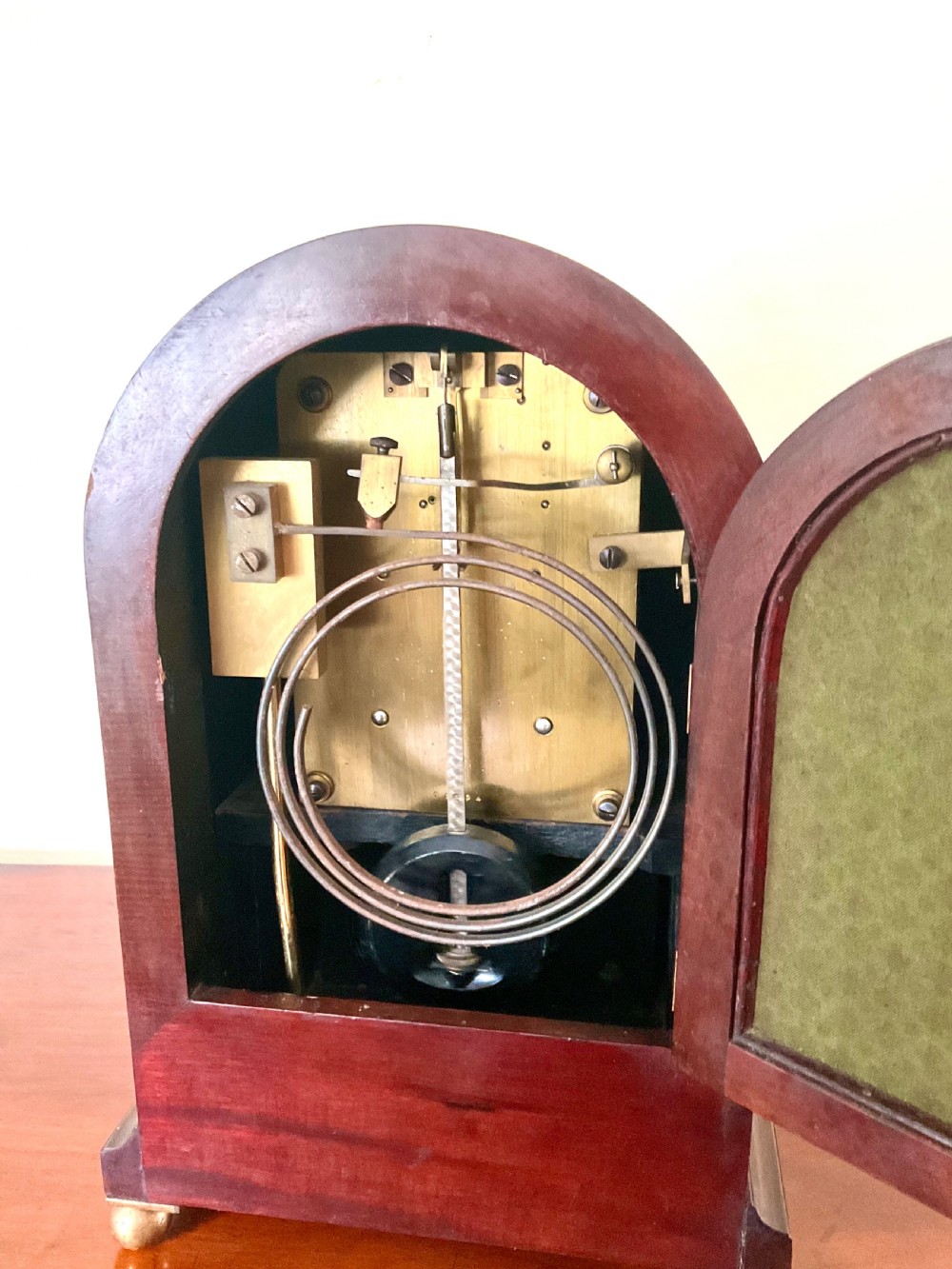 An English mahogany bracket clock featuring an arched top, white dial with Roman numerals, brass bezel, geometric marquetry inlay, and four brass ball feet. View V