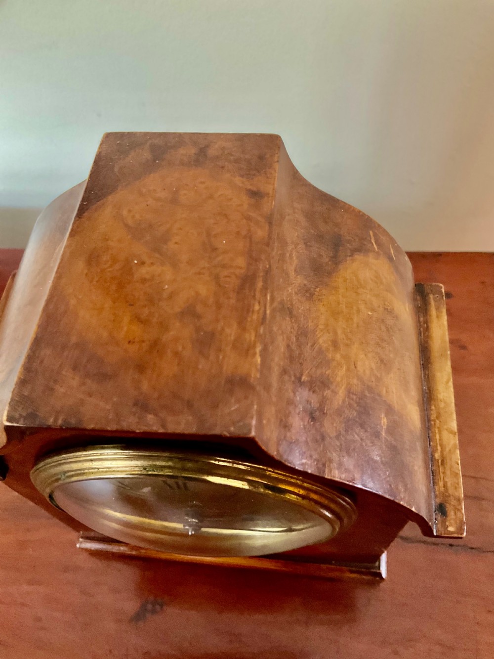 A small figured walnut mantel clock featuring an arched timber case, a brass-framed dial, and black Roman numerals. View II