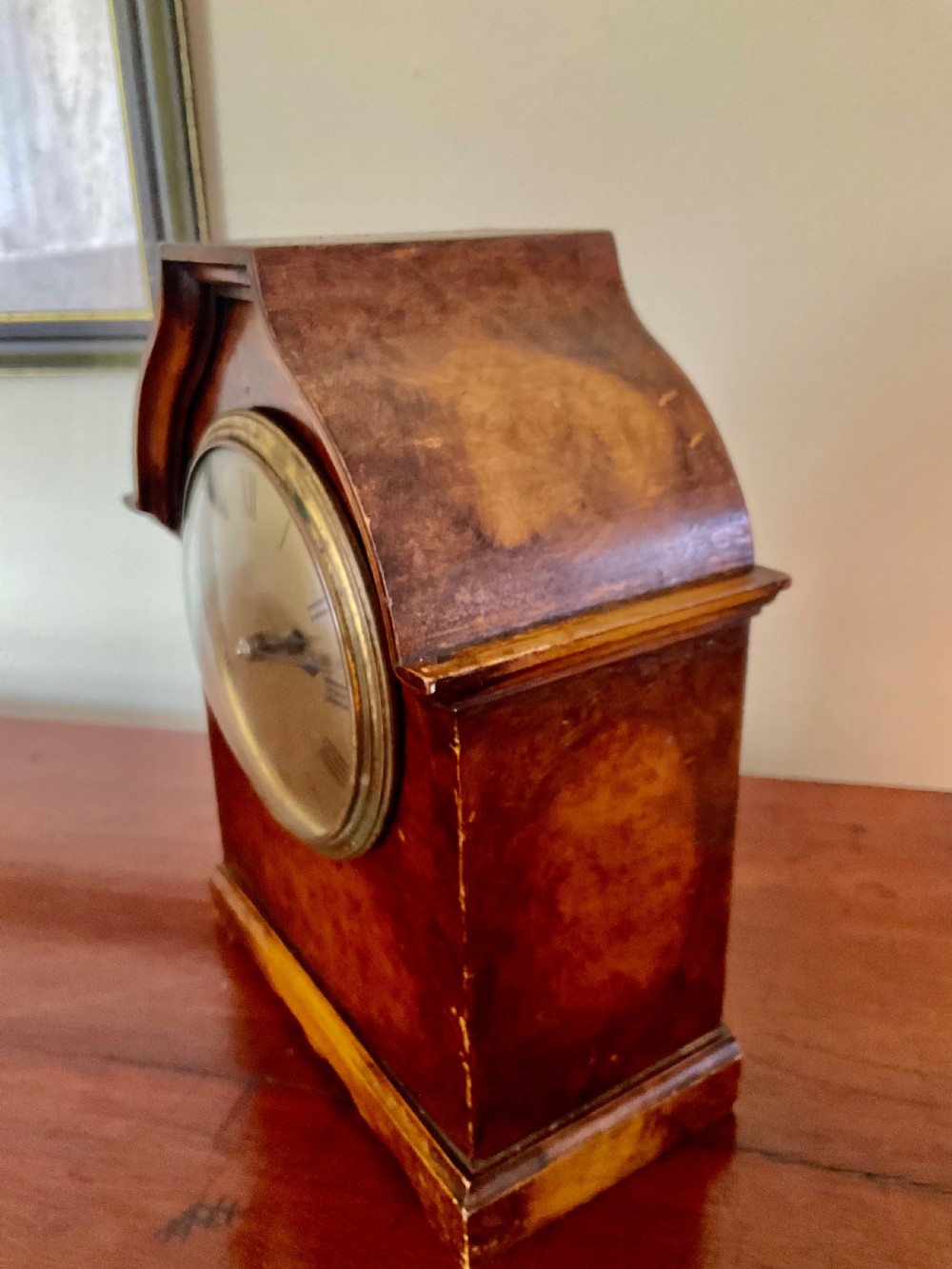 A small figured walnut mantel clock featuring an arched timber case, a brass-framed dial, and black Roman numerals. View IV