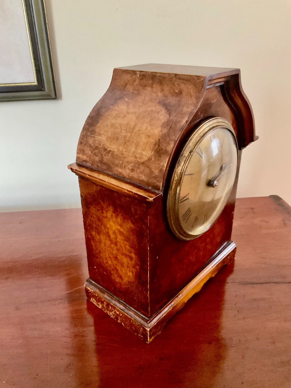 A small figured walnut mantel clock featuring an arched timber case, a brass-framed dial, and black Roman numerals. View V