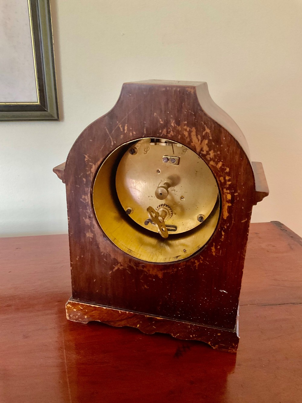 A small figured walnut mantel clock featuring an arched timber case, a brass-framed dial, and black Roman numerals. View VIII