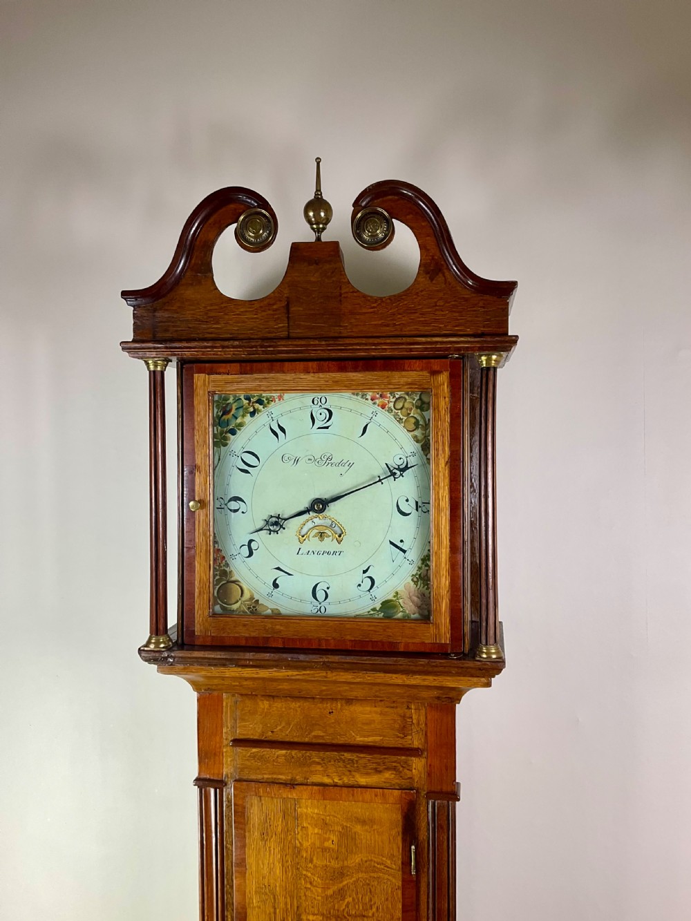 An 18th-century Georgian oak and mahogany longcase clock featuring a swan-neck pediment, fluted columns, and a painted dial face signed by Preddy of Langport. View II