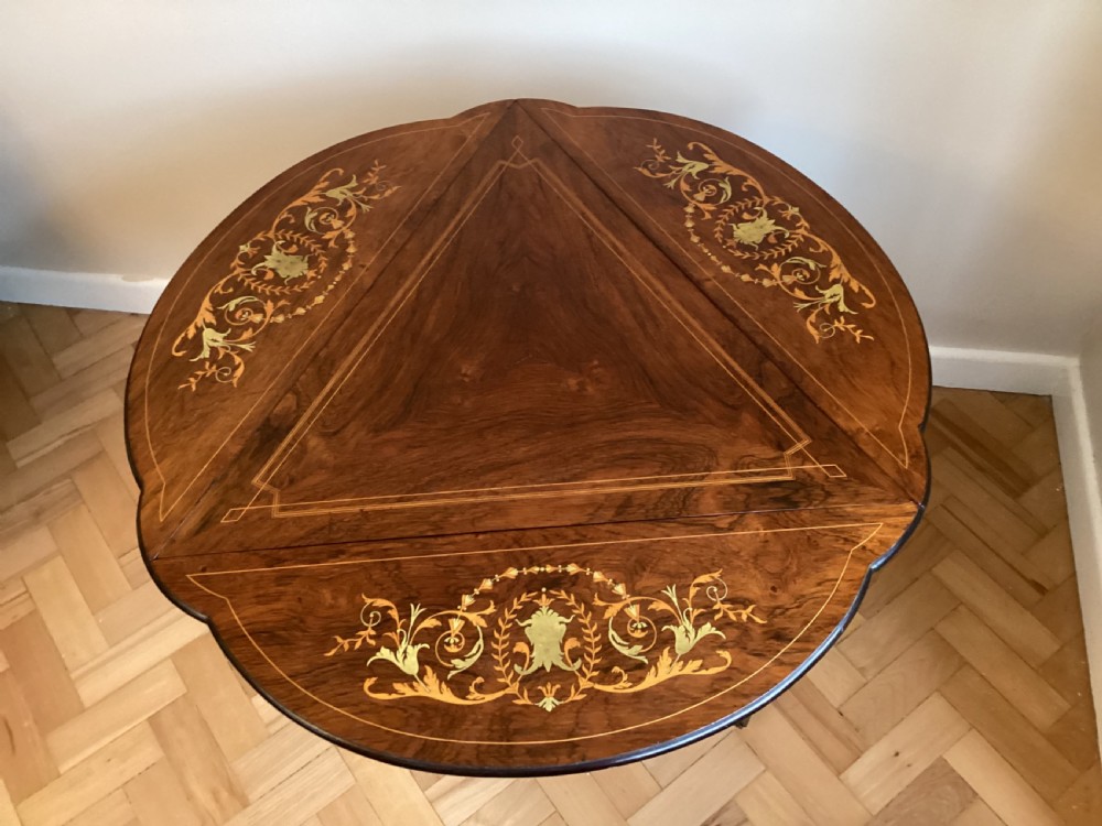 An Edwardian rosewood drop flap occasional table featuring intricate floral marquetry inlay, a lower tier shelf, and curved legs on brass castors. View II